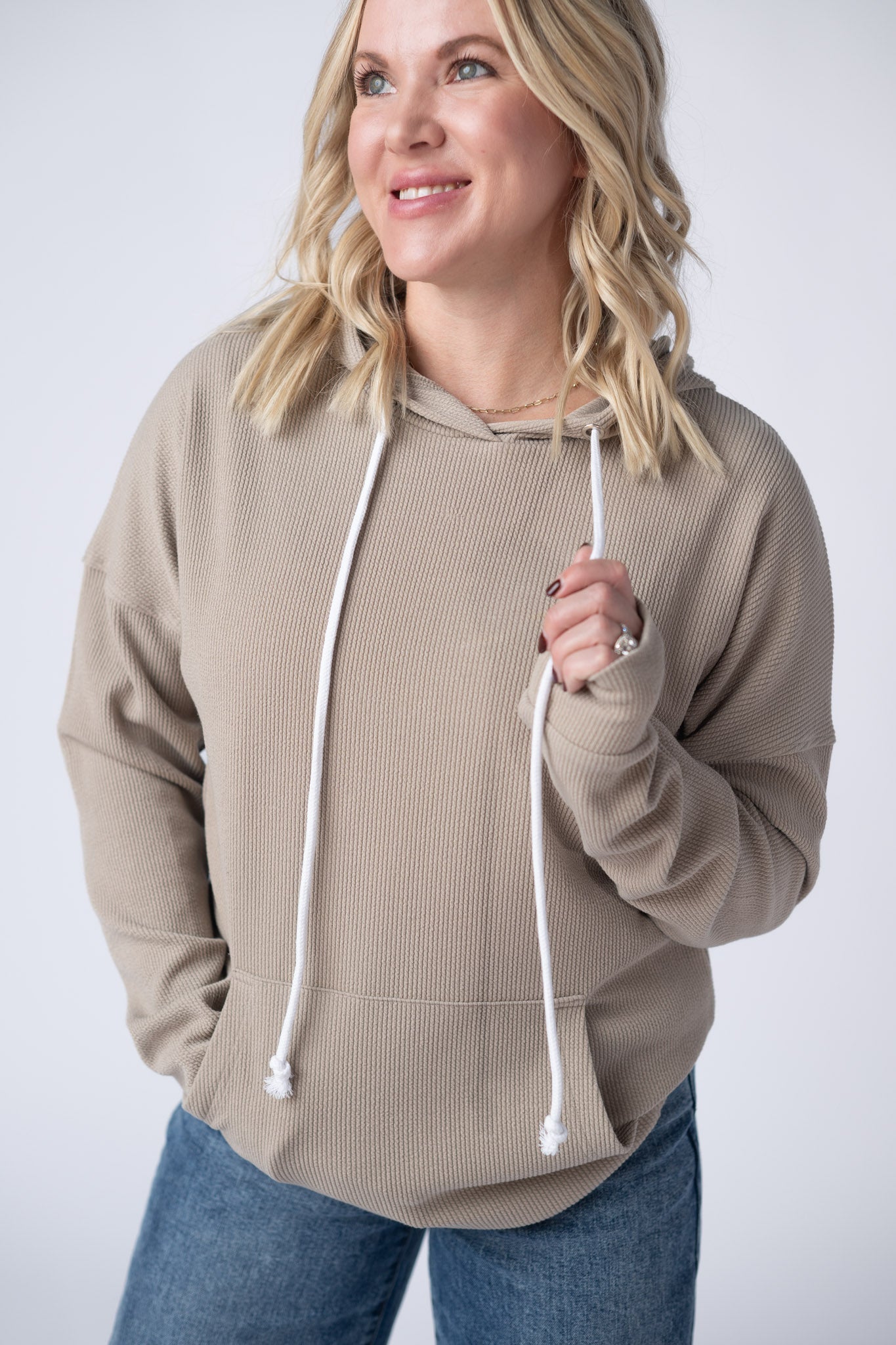  Woman wearing a mocha brown Kacey Ribbed Hoodie with white drawstrings, kangaroo pocket, and ribbed texture, paired with jeans