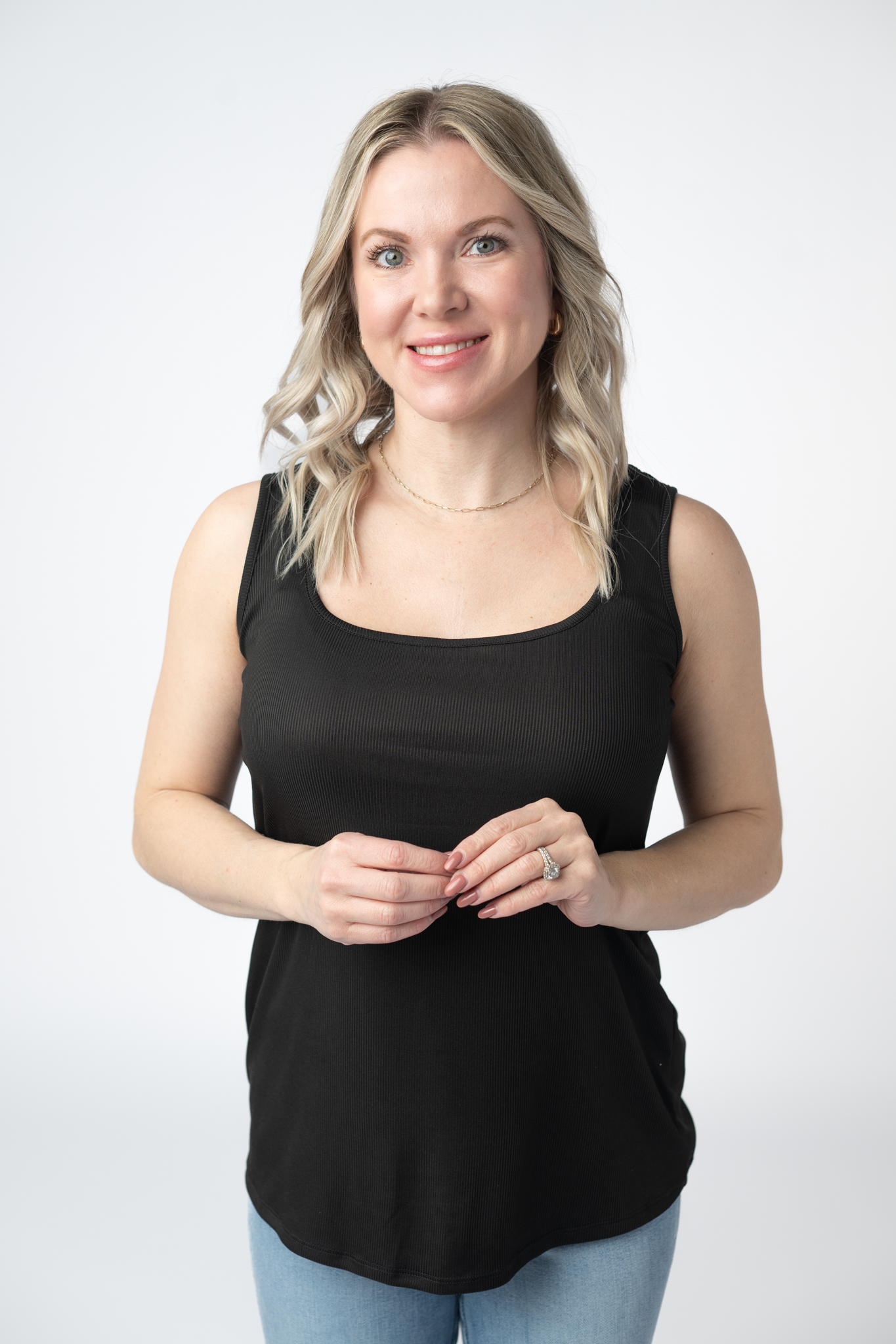Woman wearing a black Rachel Ribbed Tank with scoop neck and curved hem in lightweight ribbed fabric, paired with light wash jeans