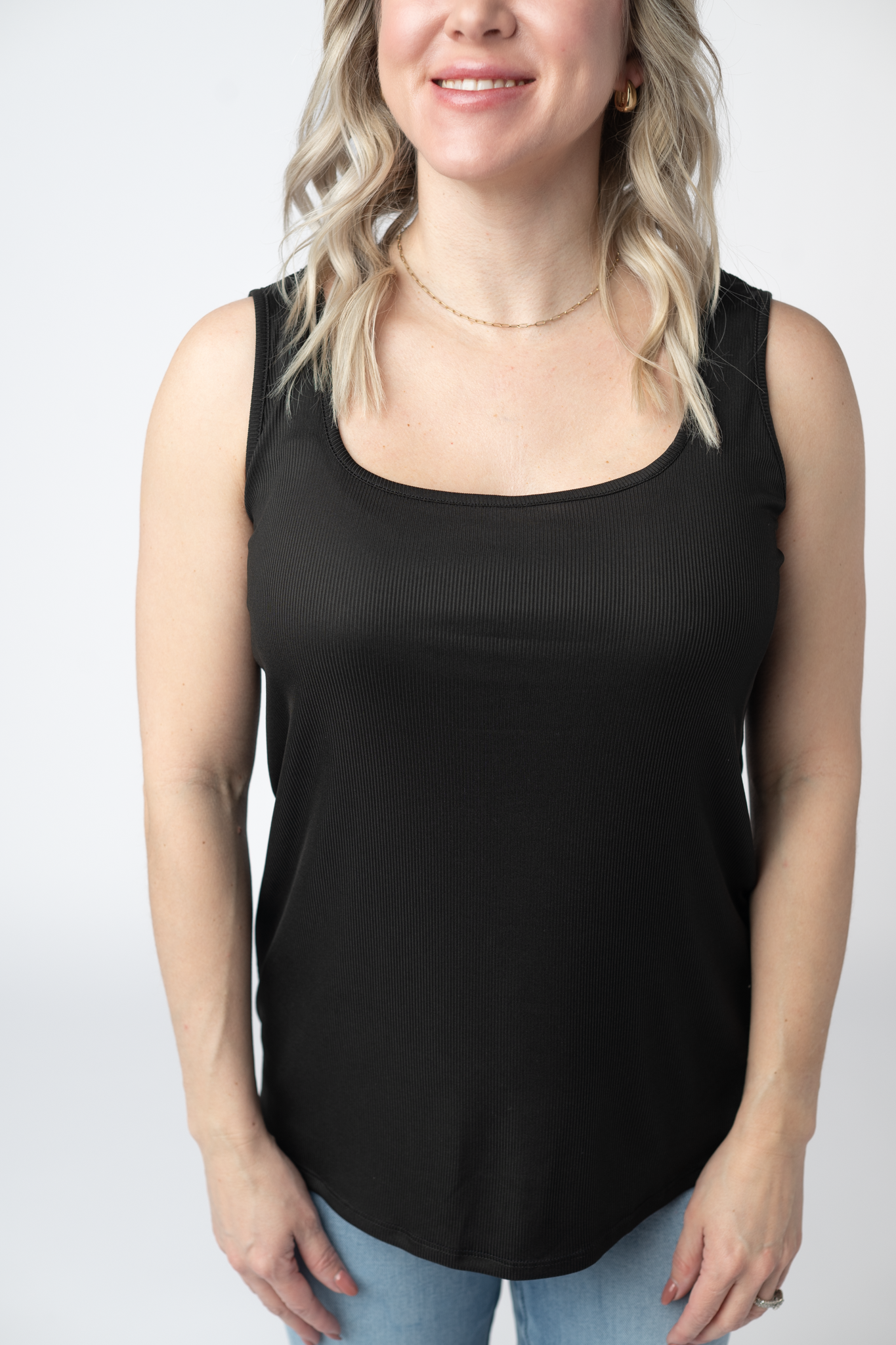 Woman wearing a black Rachel Ribbed Tank with scoop neck and curved hem in lightweight ribbed fabric, paired with light wash jeans