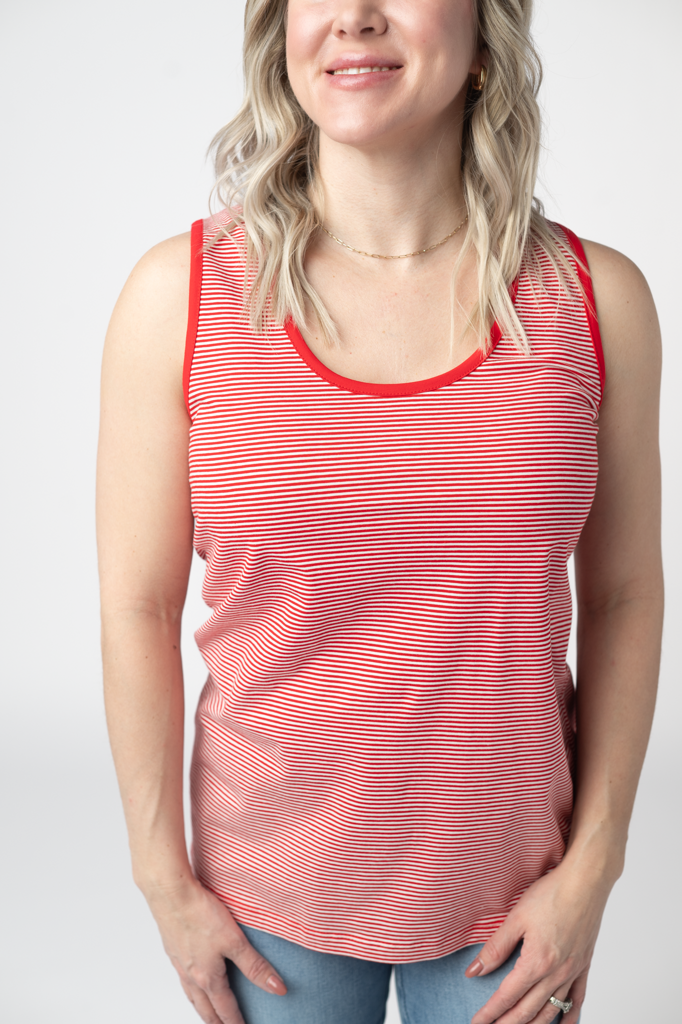 Woman wearing a red and white micro striped tank top with solid red contrast trim at neckline and armholes, paired with light wash jeans