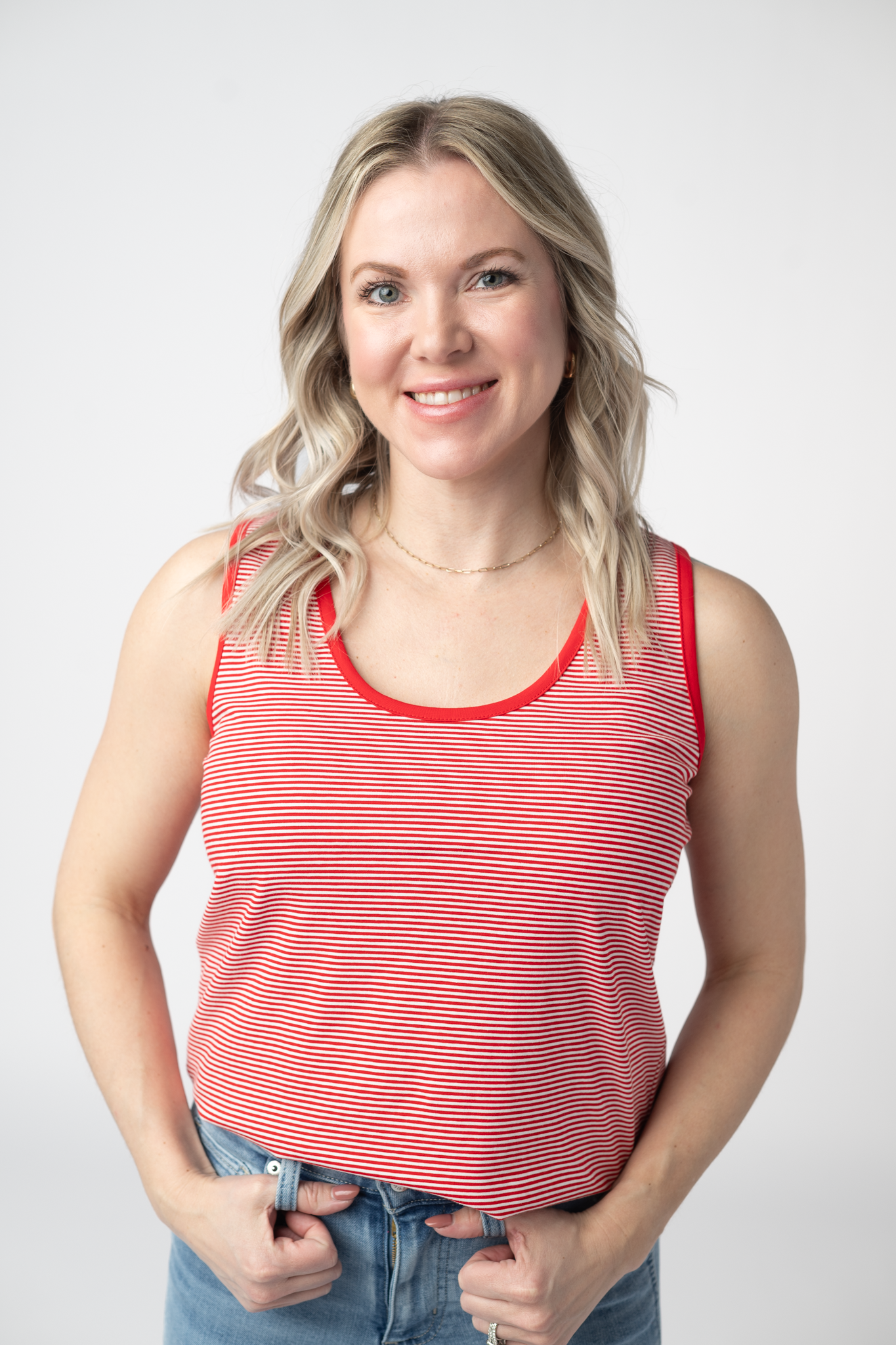 Woman wearing a red and white micro striped tank top with solid red contrast trim at neckline and armholes, paired with light wash jeans