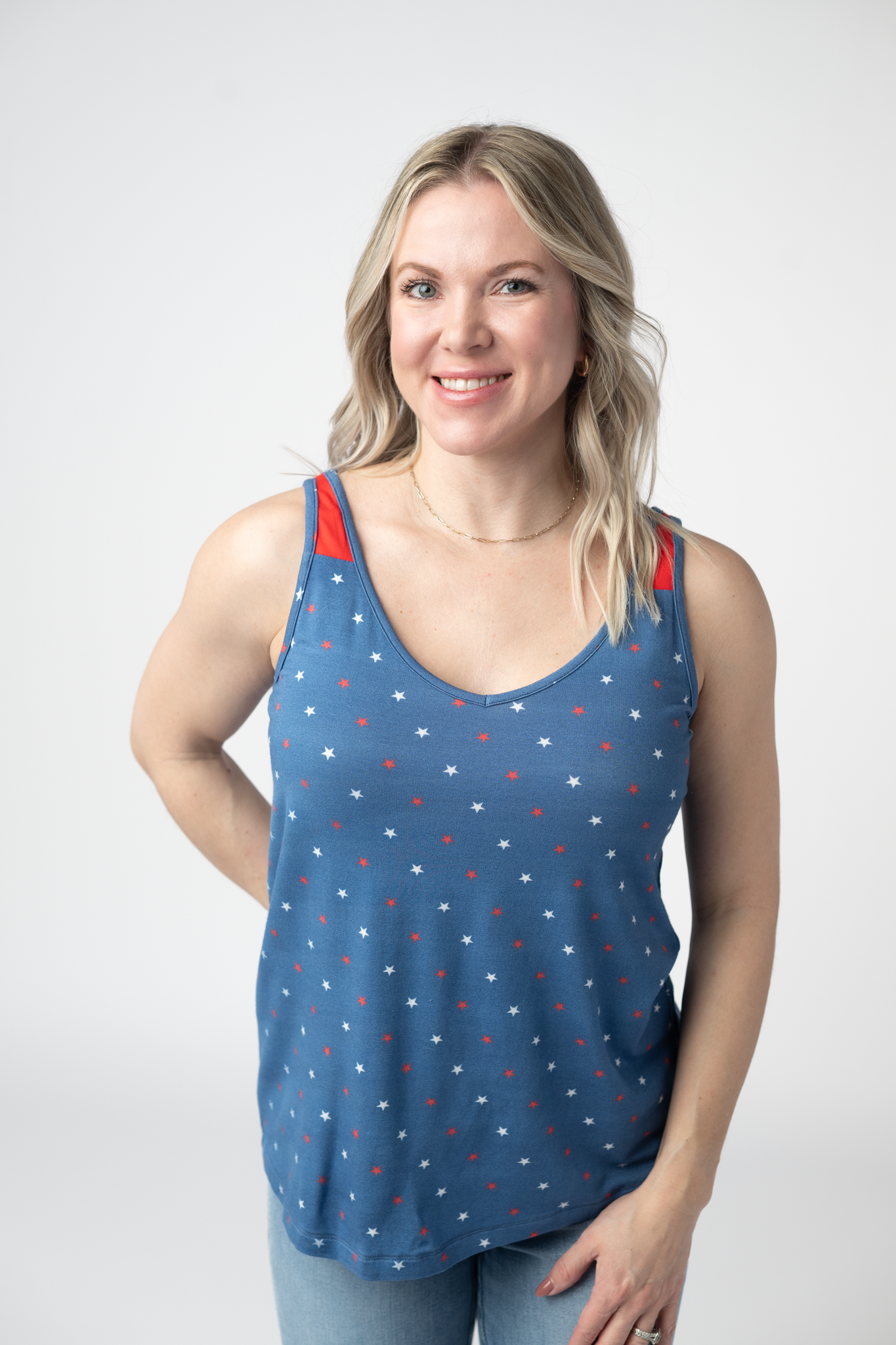 Woman wearing a blue patriotic tank top with red and white star print and contrast red straps, paired with light wash jeans
