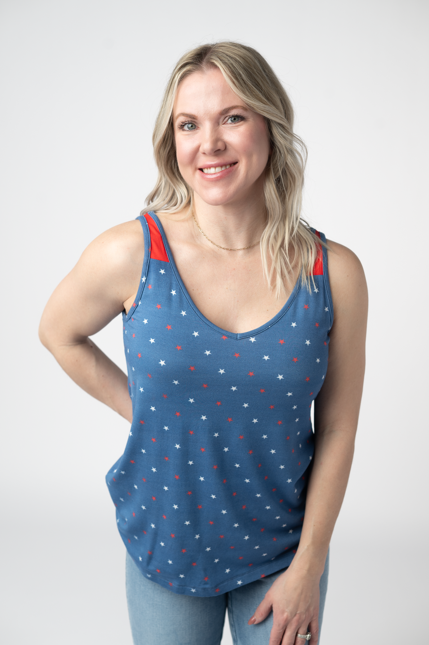 Woman wearing a blue patriotic tank top with red and white star print and contrast red straps, paired with light wash jeans