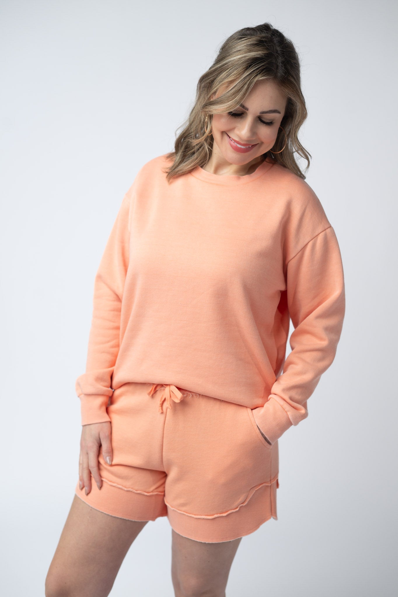 Women's vintage wash pullover in Spring Peach with crew neck, relaxed fit, and raw edge hem details, paired with matching drawstring shorts