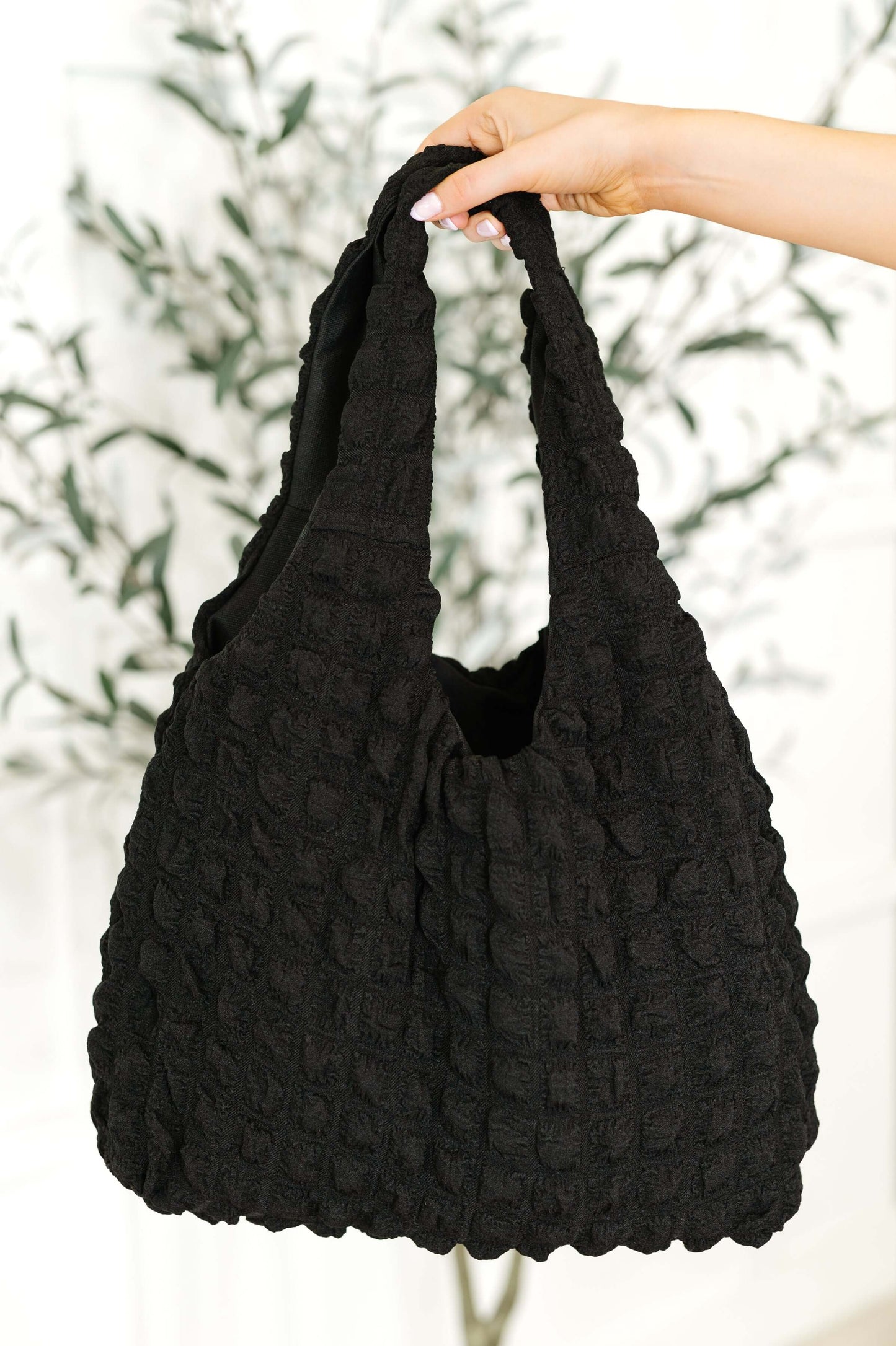Hand holding black textured quilted tote bag with soft bubble design