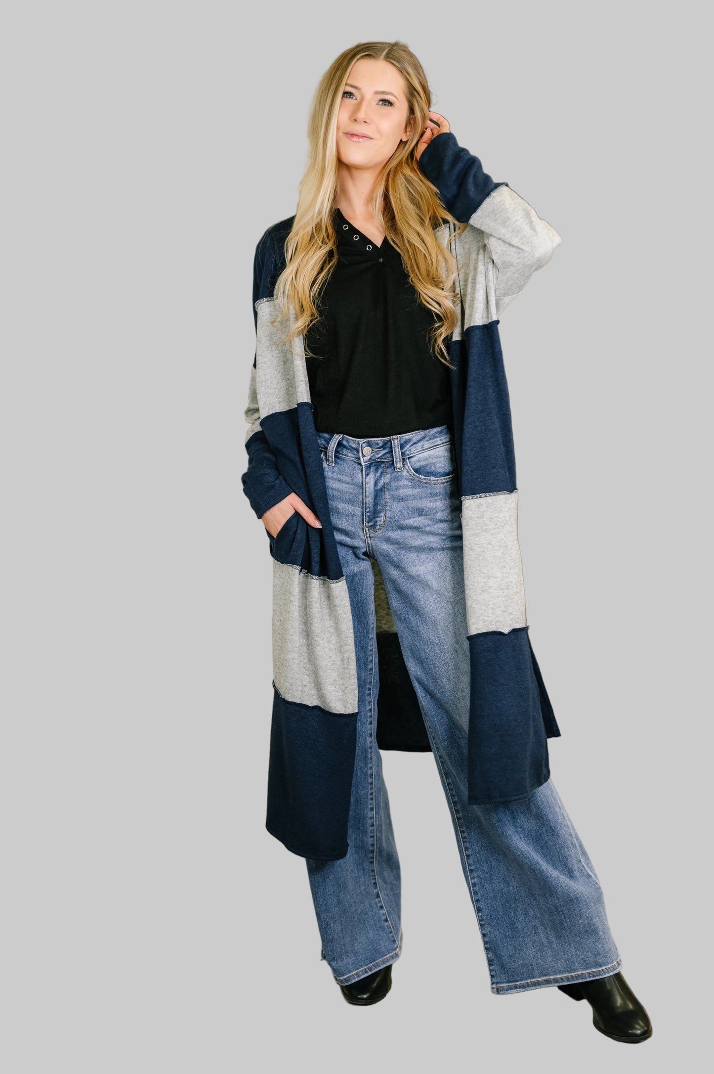 Women's longline duster cardigan in navy and heather gray colorblock stripes with open front, drop shoulders, and side pockets styled with black top and flare jeans