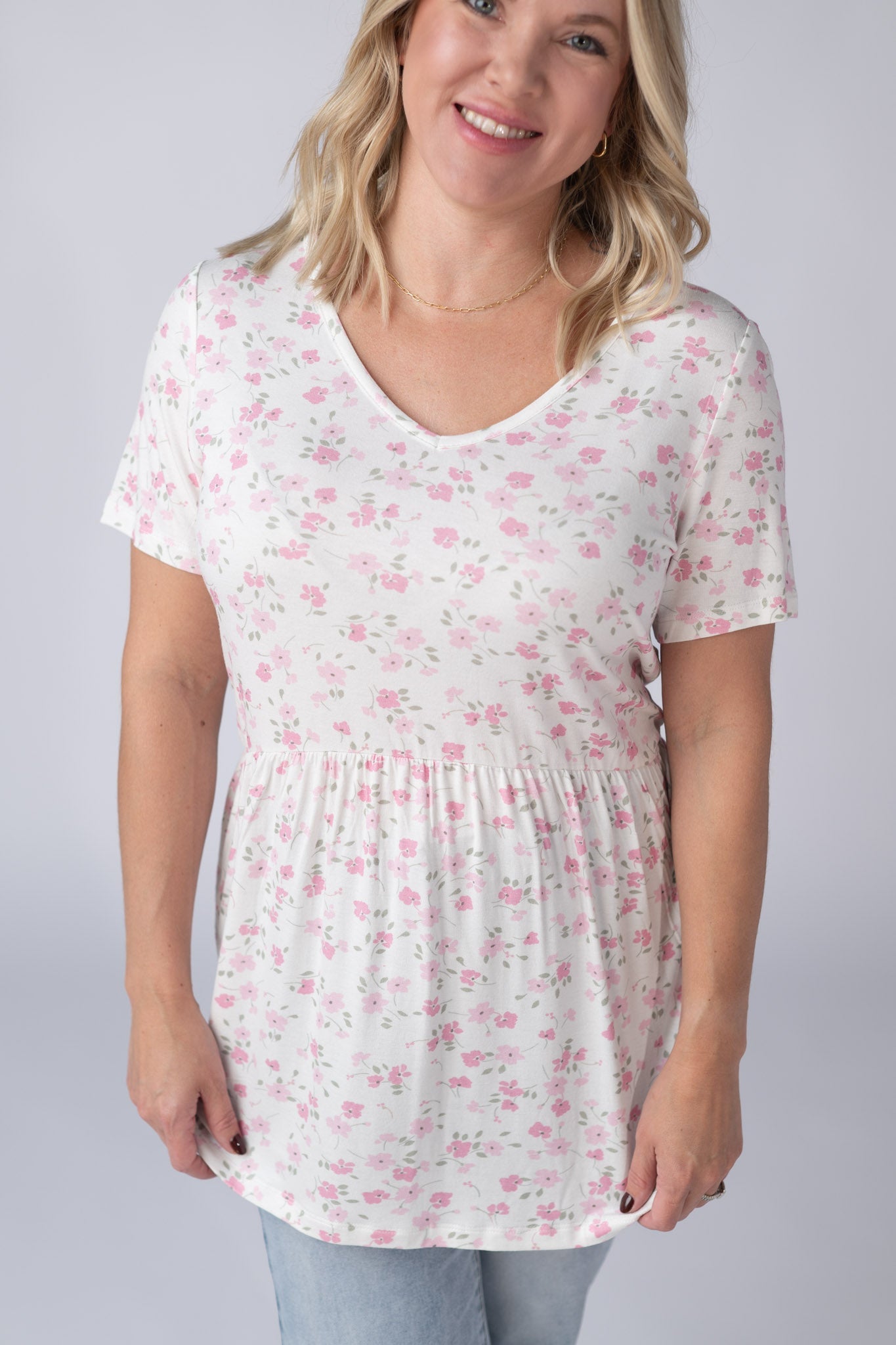 Woman wearing a white Sarah Ruffle Top with delicate pink floral print and gray leaves, featuring a v-neckline and gathered waist