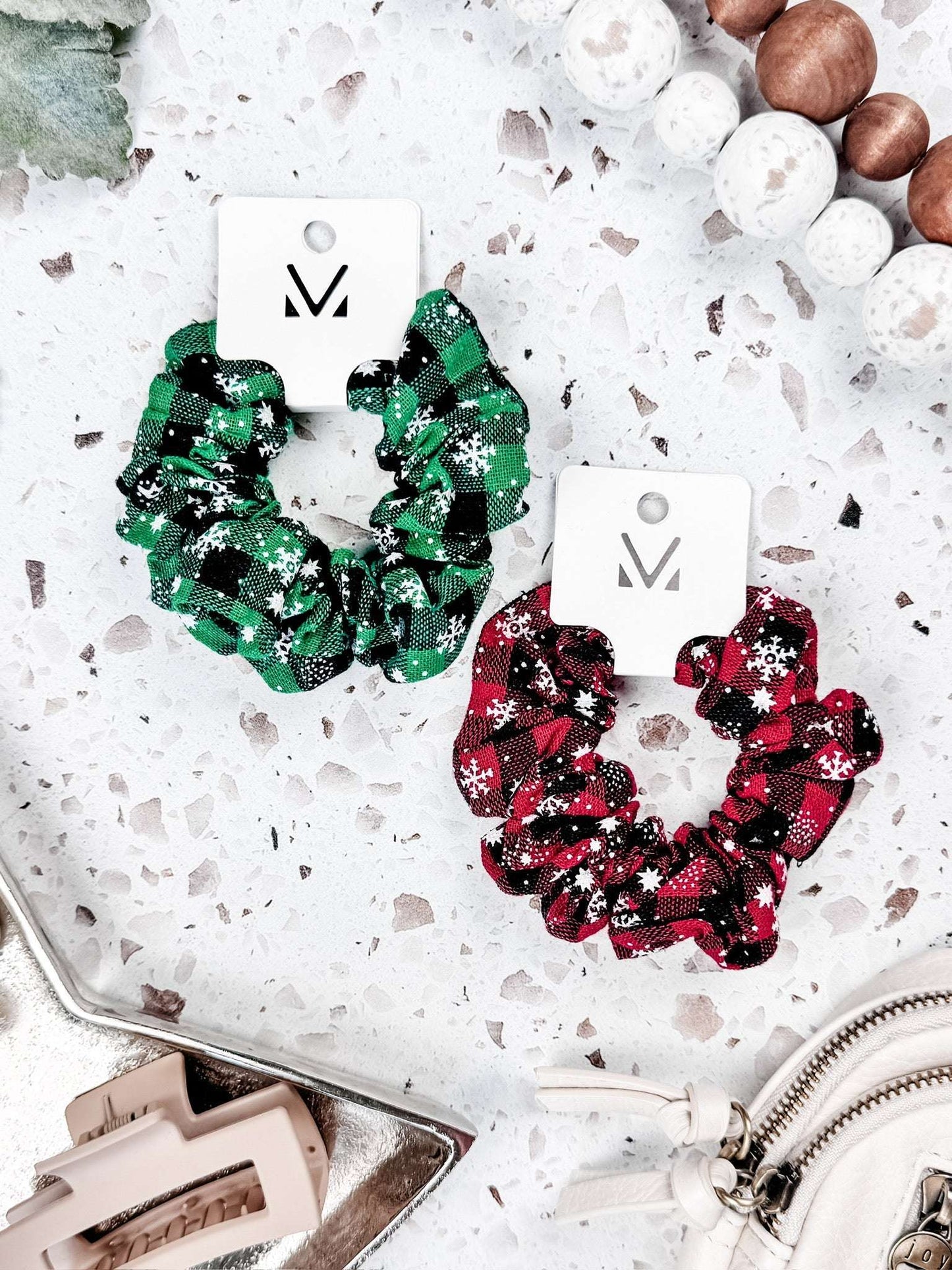 Set of two holiday plaid scrunchies with snowflake print—one red, one green—on a white terrazzo background