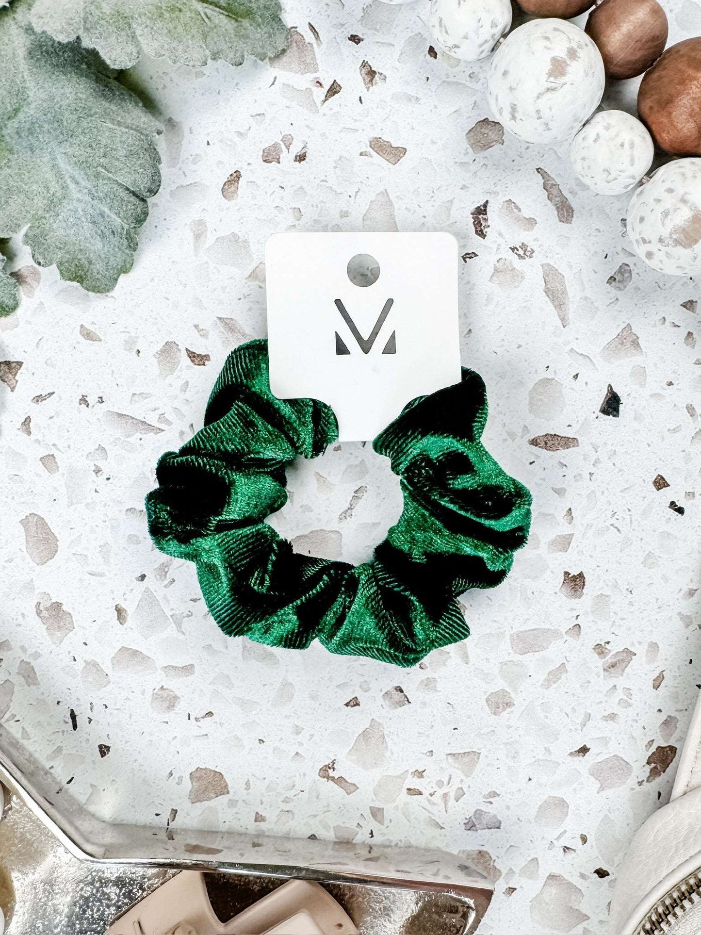 Emerald green velvet scrunchie on white speckled surface with decorative accents