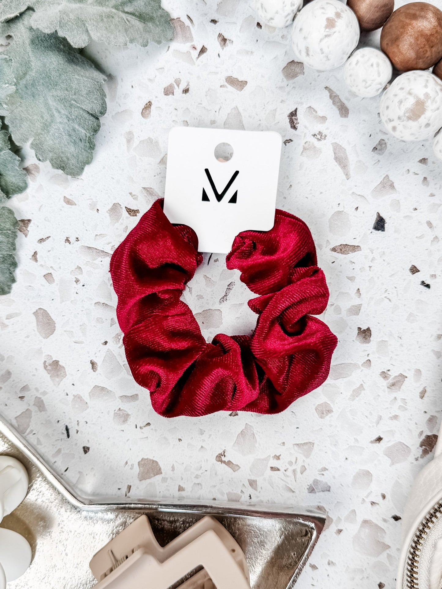 Red velvet scrunchie on speckled white background with winter decor
