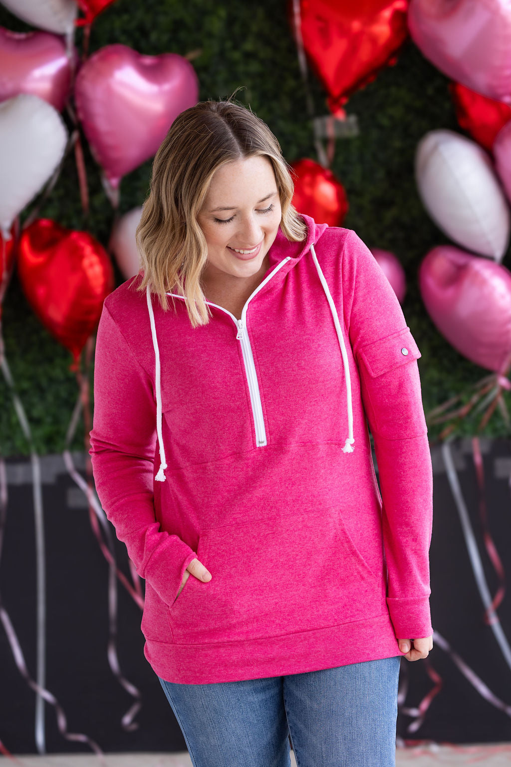 Woman wearing hot pink half-zip hoodie with kangaroo pocket, white zipper and drawstrings, and cozy hood