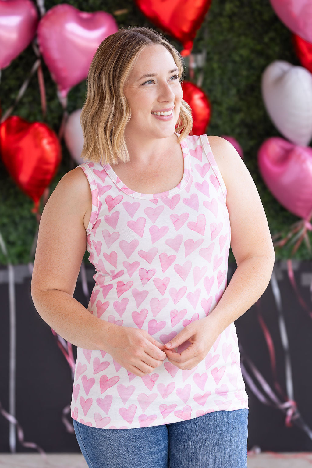Woman wearing ribbed tank top with pink watercolor hearts print, scoop neckline, and fitted silhouette