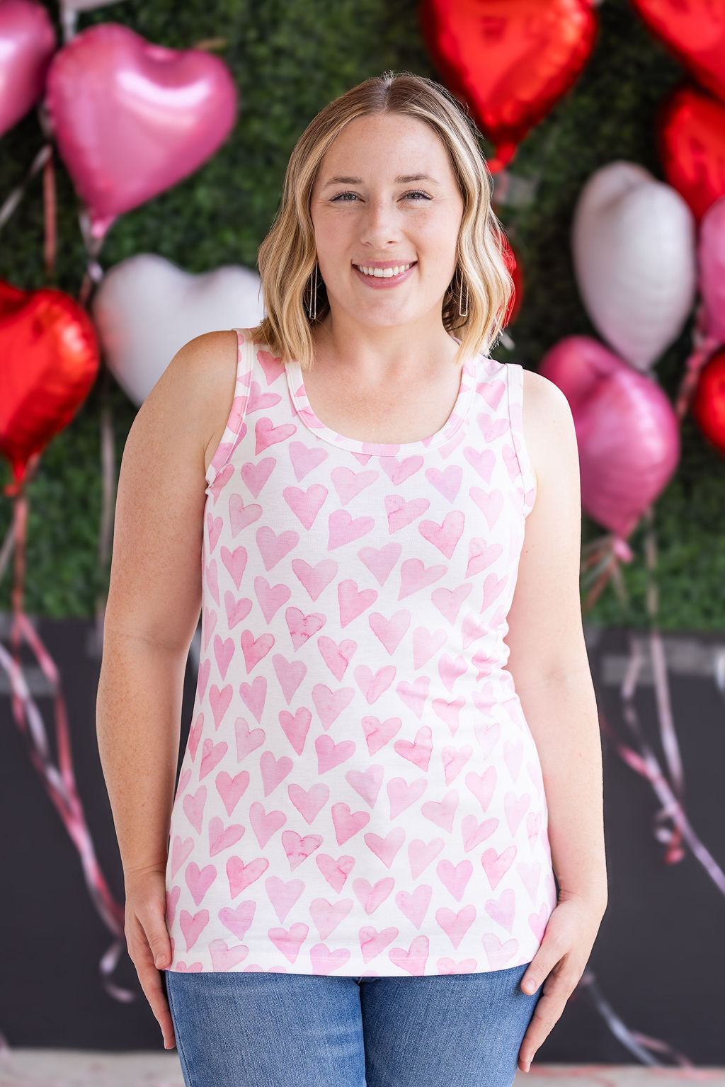 Woman wearing ribbed tank top with pink watercolor hearts print, scoop neckline, and fitted silhouette