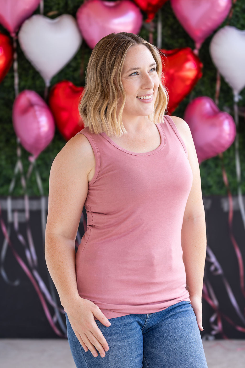 Woman wearing dusty rose ribbed tank top with scoop neckline and fitted silhouette