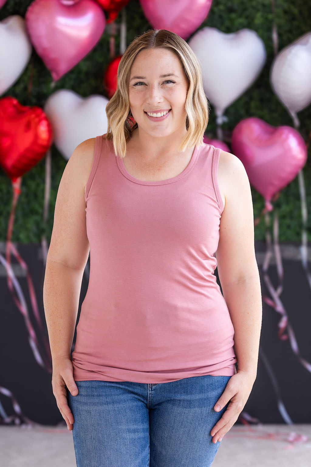 Woman wearing dusty rose ribbed tank top with scoop neckline and fitted silhouette