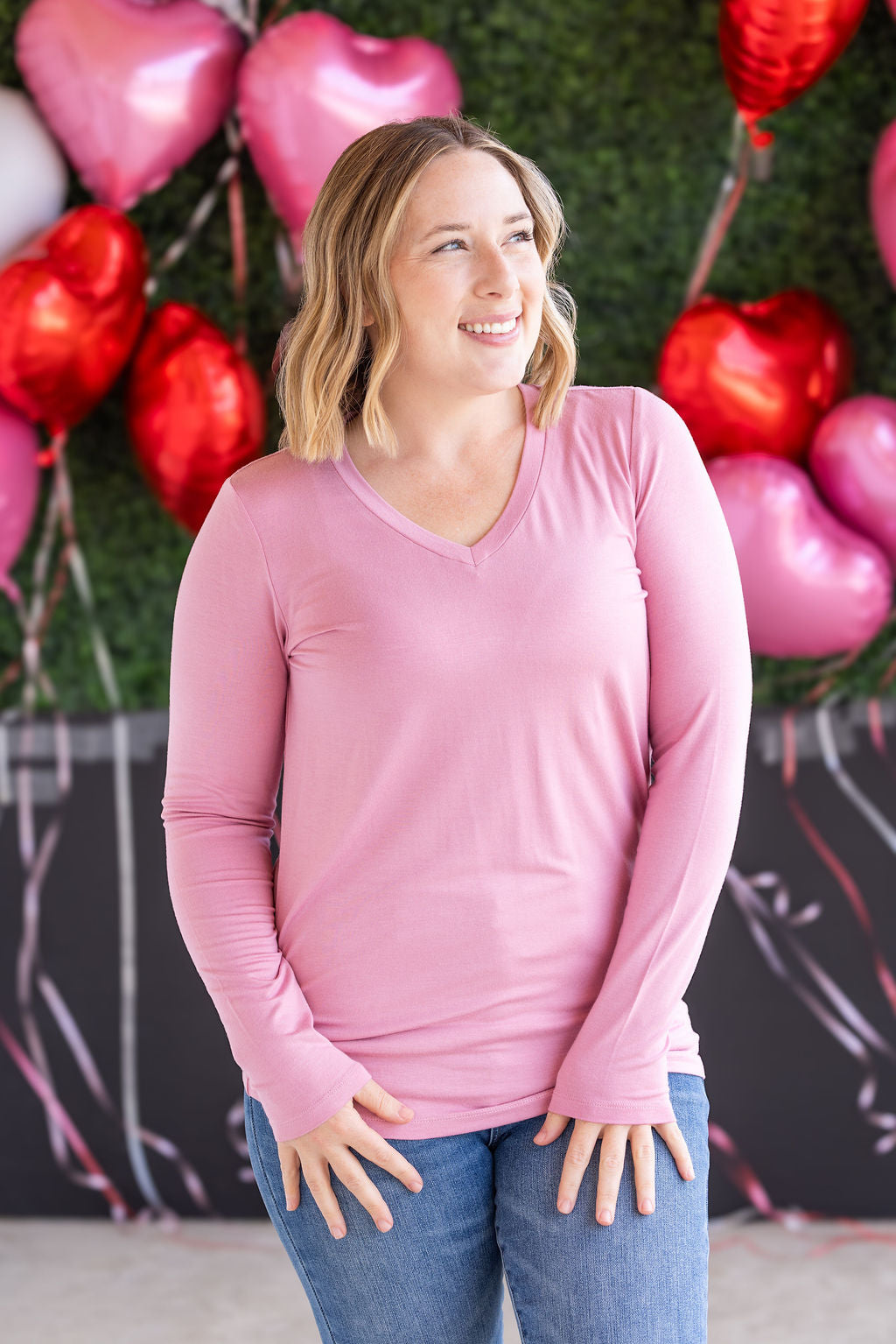 Woman wearing long sleeve v-neck top in soft rose pink with fitted silhouette and flattering v-neckline.