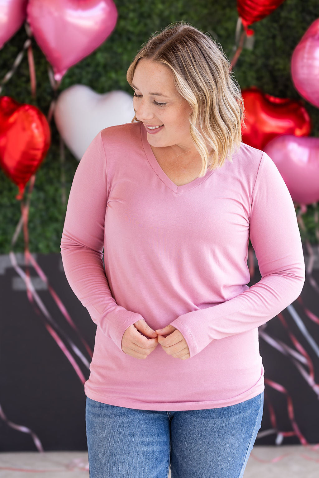 Woman wearing long sleeve v-neck top in soft rose pink with fitted silhouette and flattering v-neckline