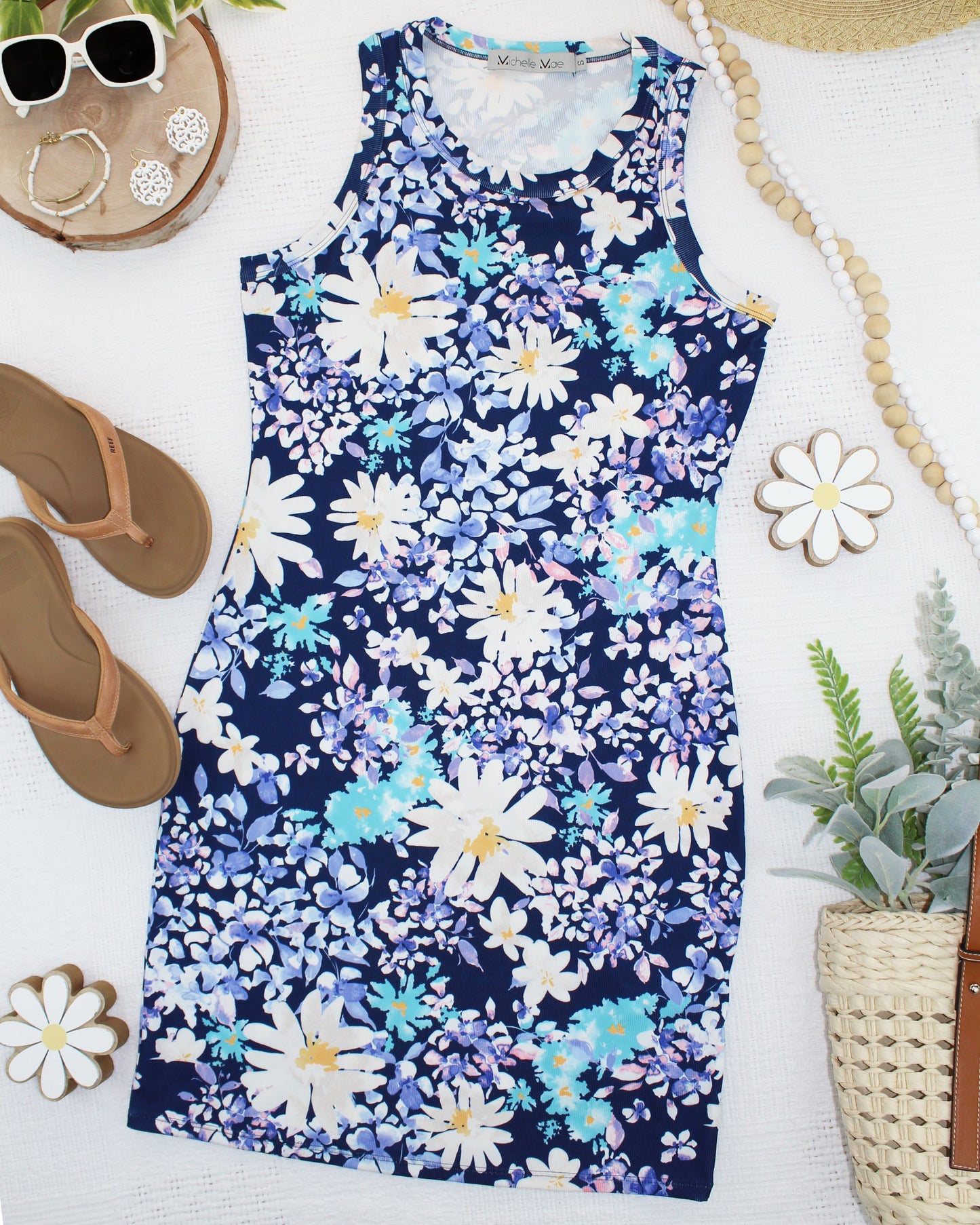 Flatlay of navy floral Mariah Ribbed Dress with white and blue daisy print, styled with tan sandals, sunglasses, and gold jewelry
