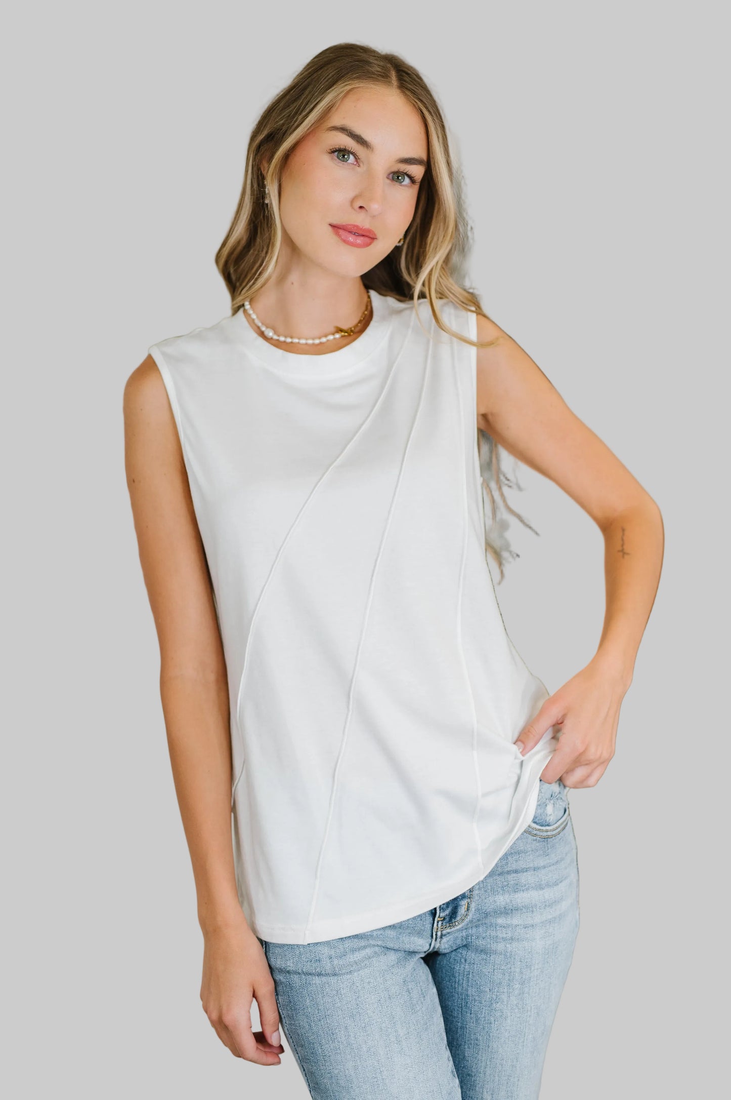 Woman wearing the One Eleven North Celeste Pleat Detail Sleeveless Top in White, a polished jersey knit sleeveless top with diagonal pleat detail and banded round neckline