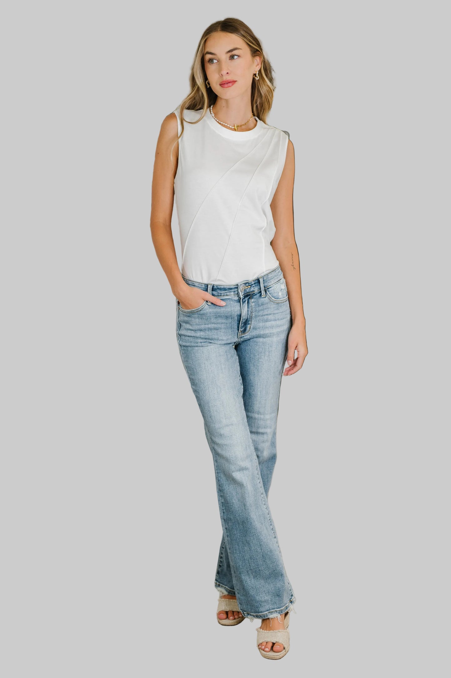 Woman wearing the One Eleven North Celeste Pleat Detail Sleeveless Top in White, a polished jersey knit sleeveless top with diagonal pleat detail and banded round neckline