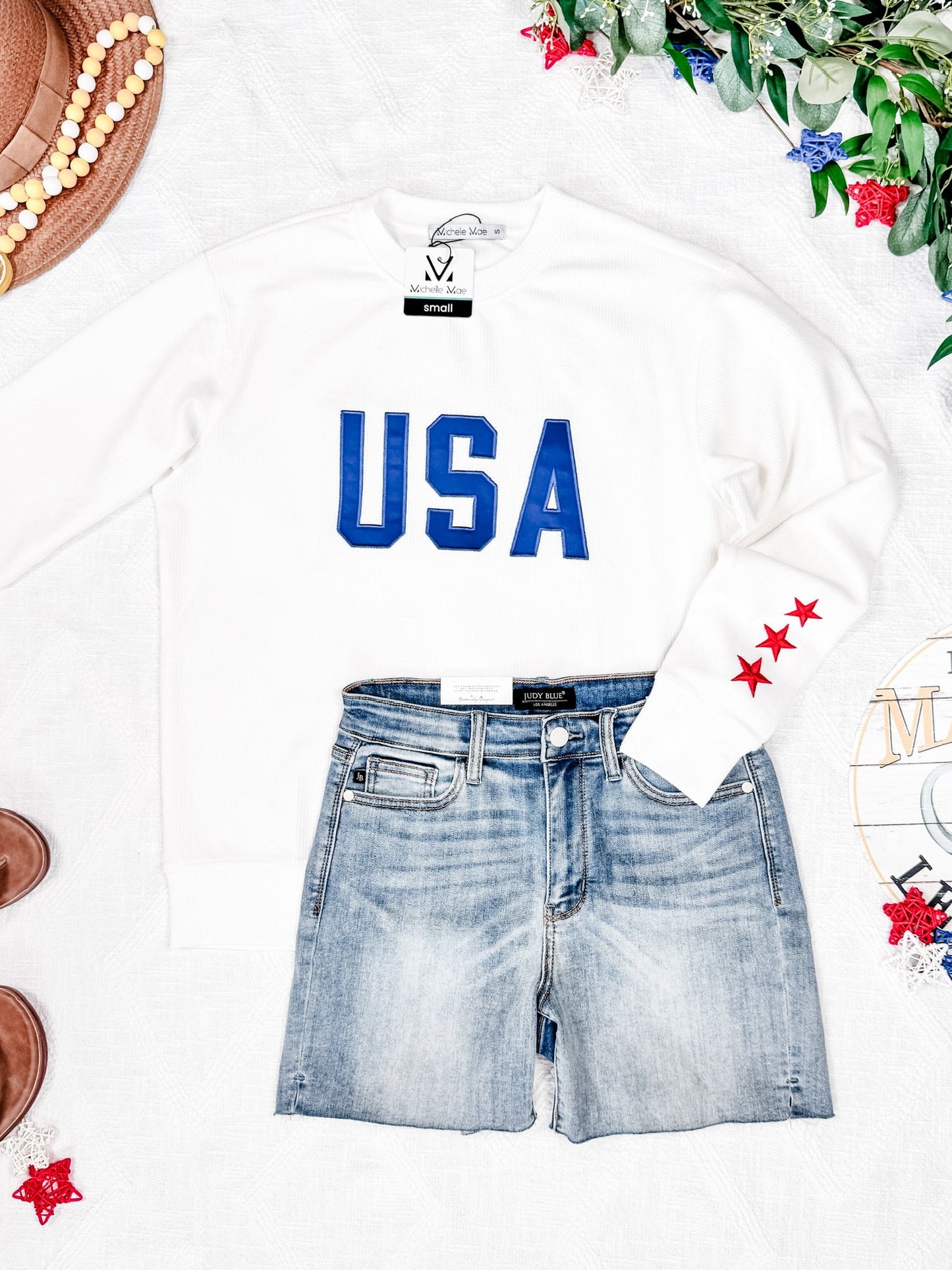 White sweatshirt with 'USA' text and denim shorts on a white background