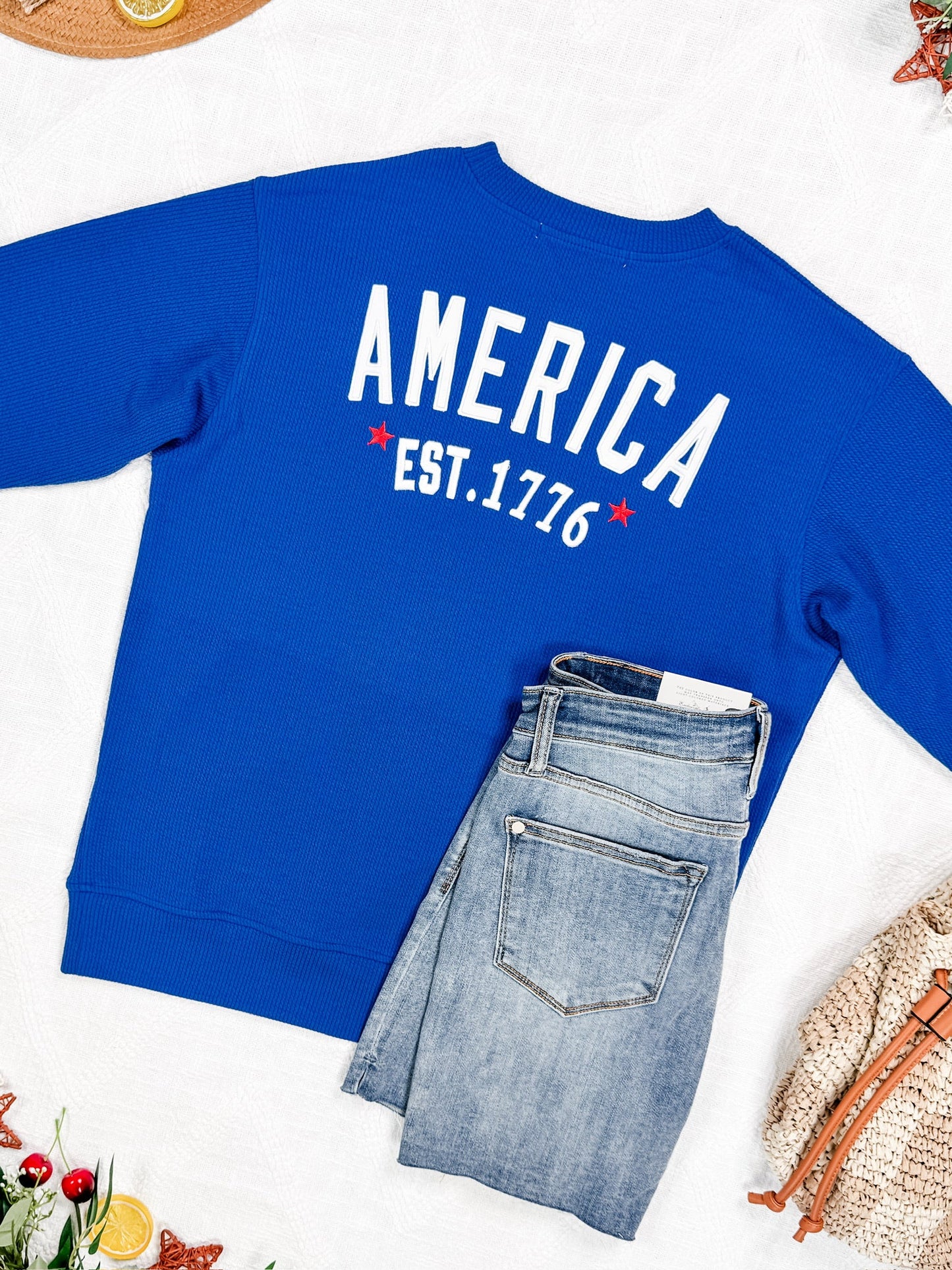 Blue sweatshirt with 'AMERICA EST. 1776' text on a white background with jeans.