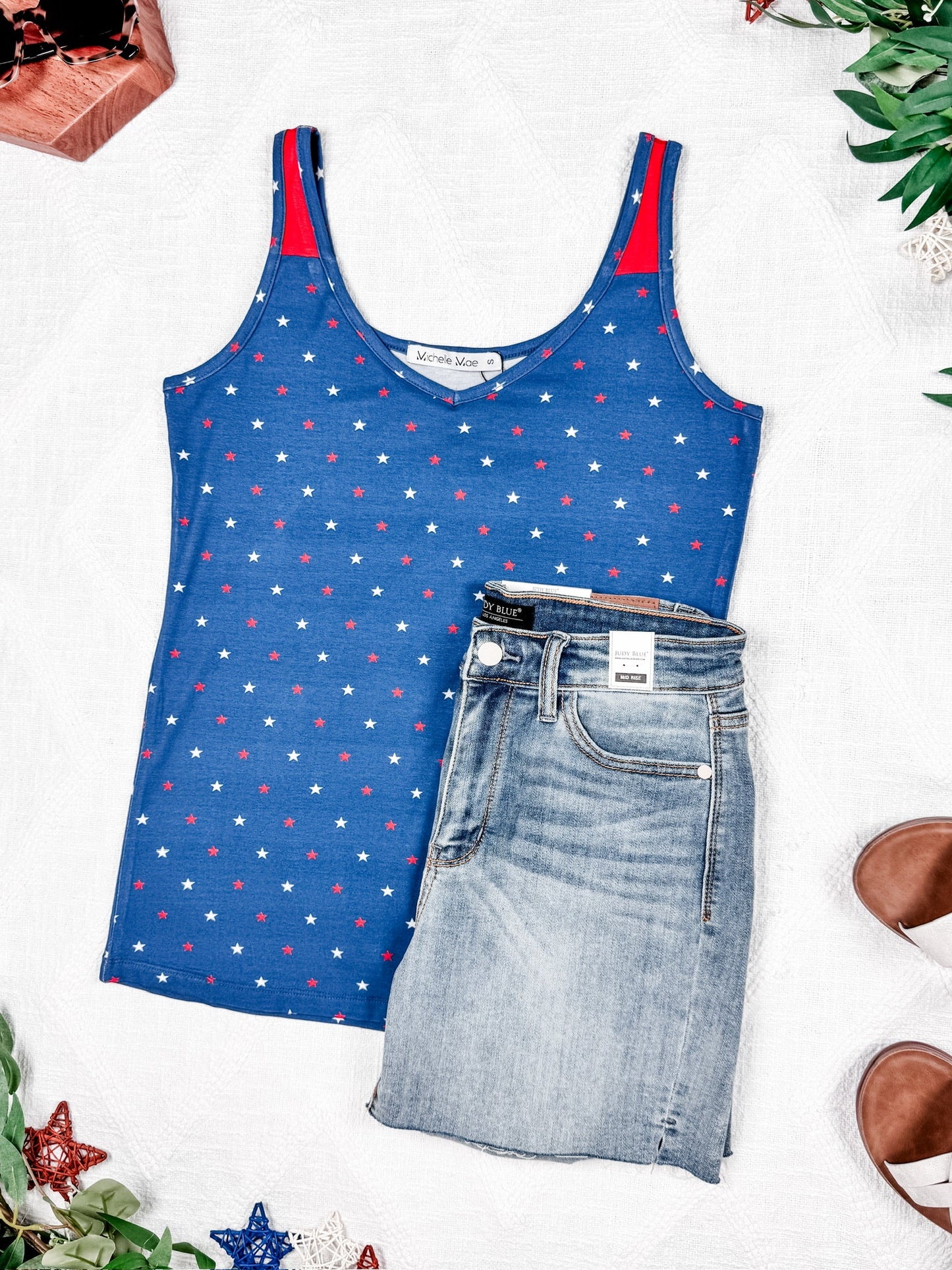 Blue tank top with red and white star pattern and denim shorts on a light background