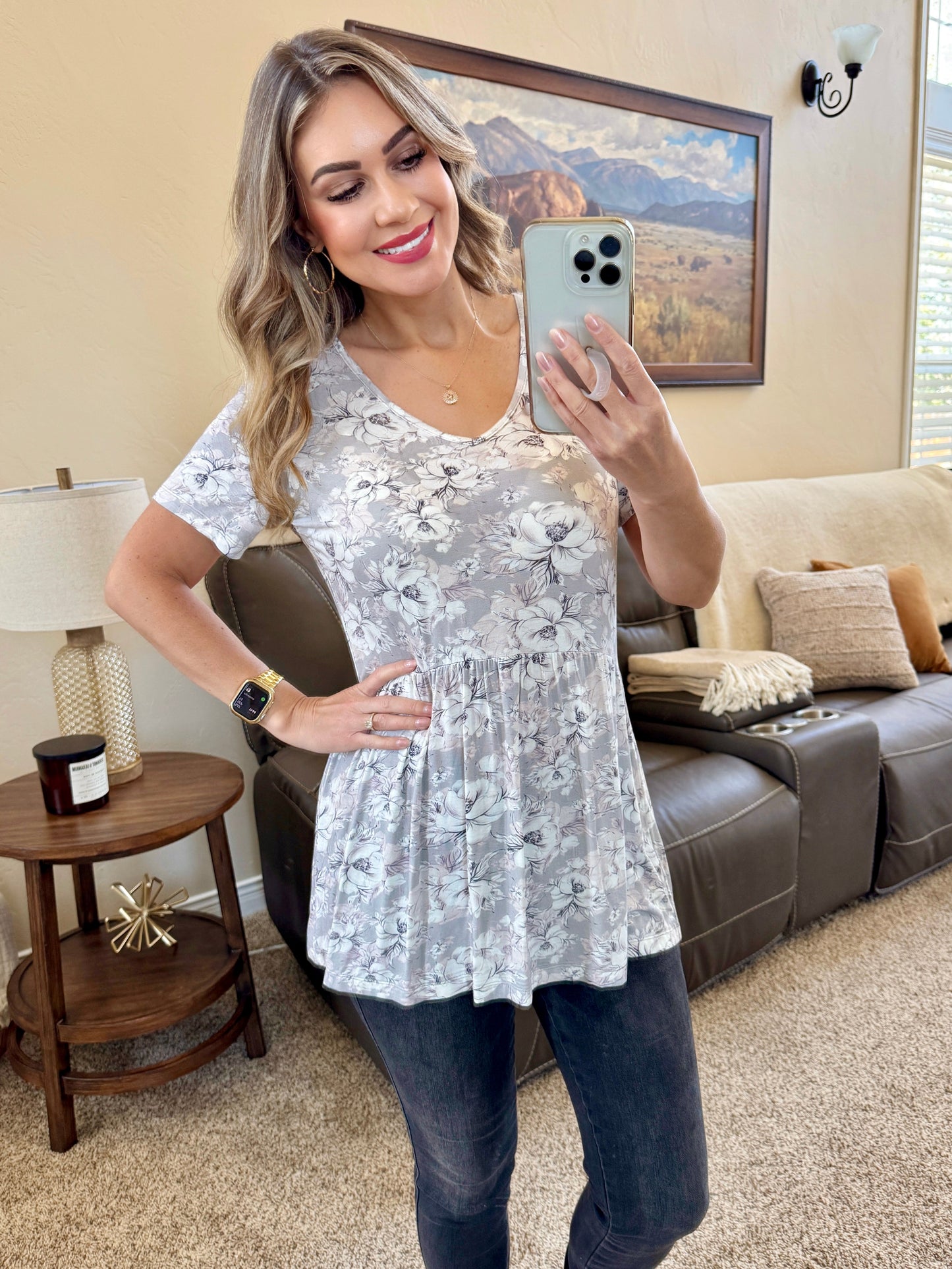 Woman wearing short sleeve ruffle top with vintage grey and white floral print and gathered ruffle hem at waist, paired with dark jeans
