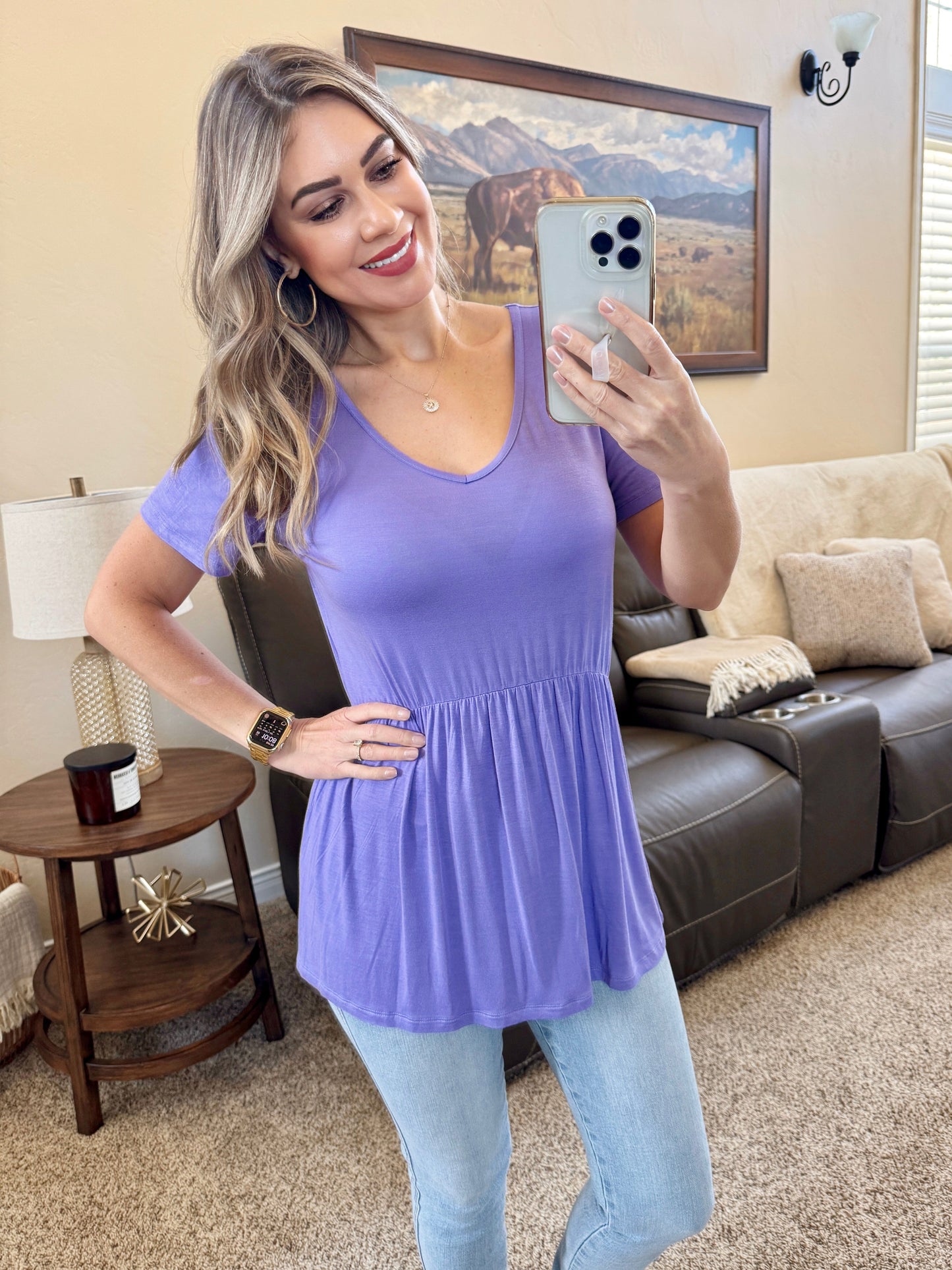 Woman wearing a periwinkle purple Sarah Ruffle Top with v-neckline and gathered waist detail, paired with jeans