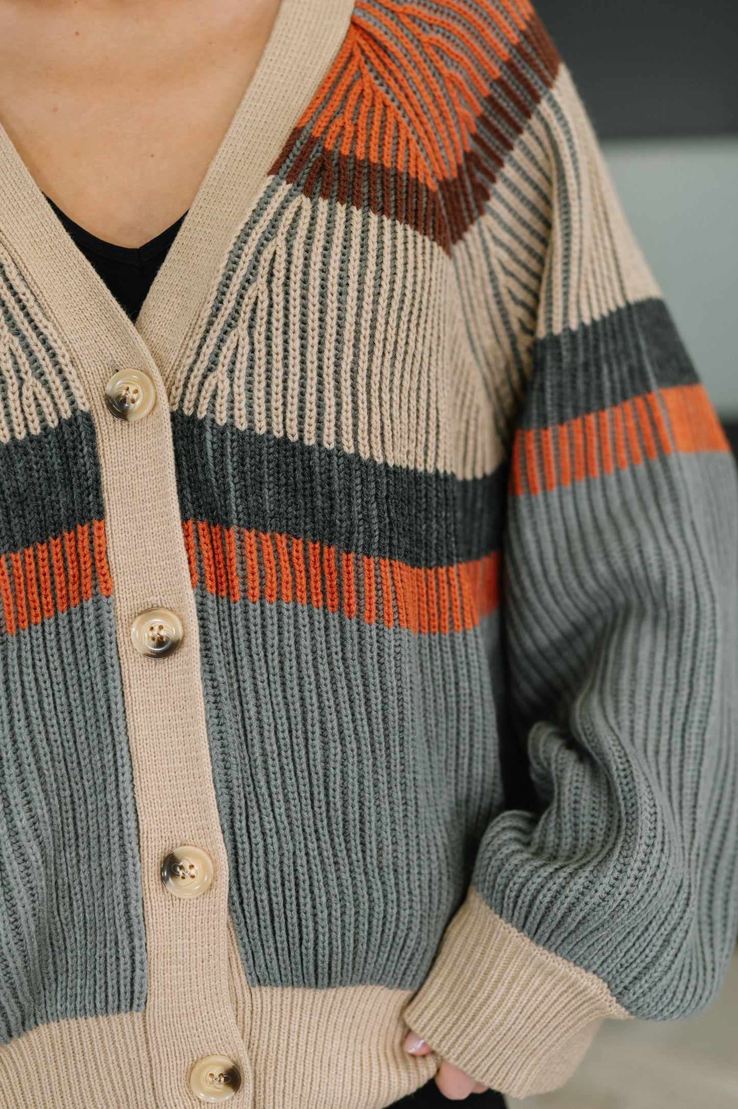 Woman wearing a striped button front cardigan in rust, cream, and grey colorblock stripes with V-neck and ribbed details, paired with black pants