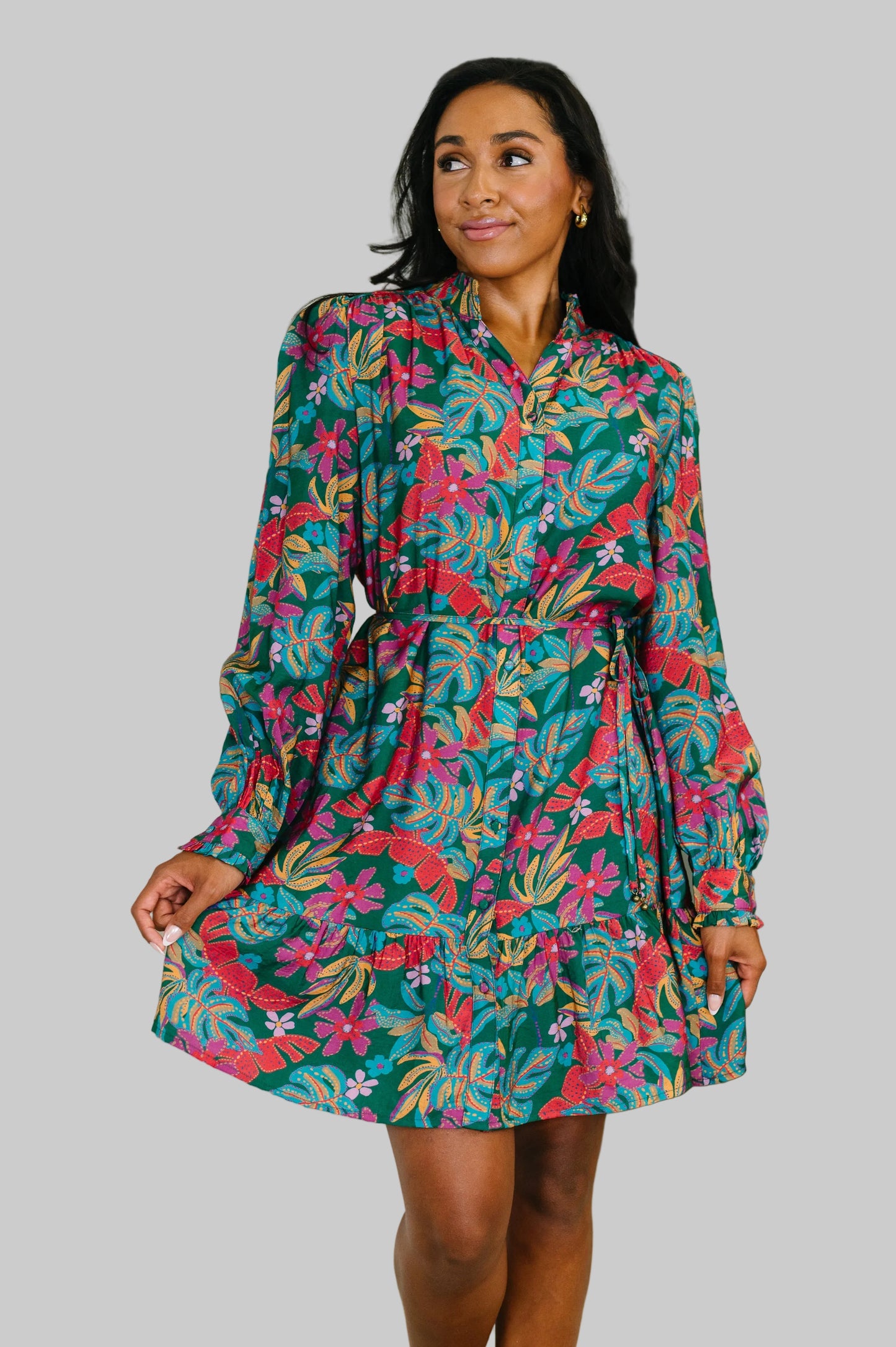 Women's tiered button-front dress in Emerald Floral with tropical print in reds, magentas, and gold, featuring ruffled v-neckline, long sleeves, waist tie, and tiered skirt