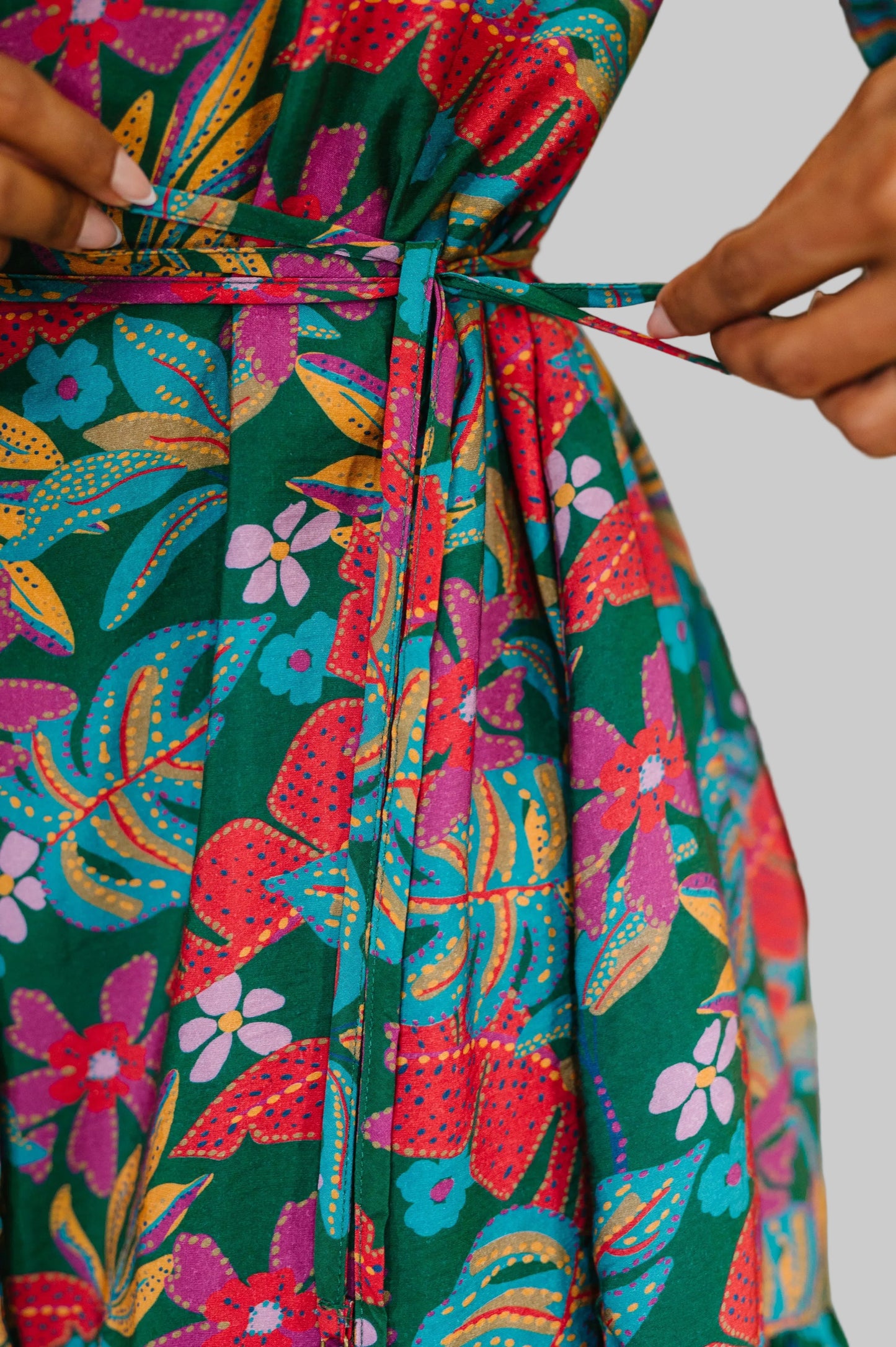 Women's tiered button-front dress in Emerald Floral with tropical print in reds, magentas, and gold, featuring ruffled v-neckline, long sleeves, waist tie, and tiered skirt