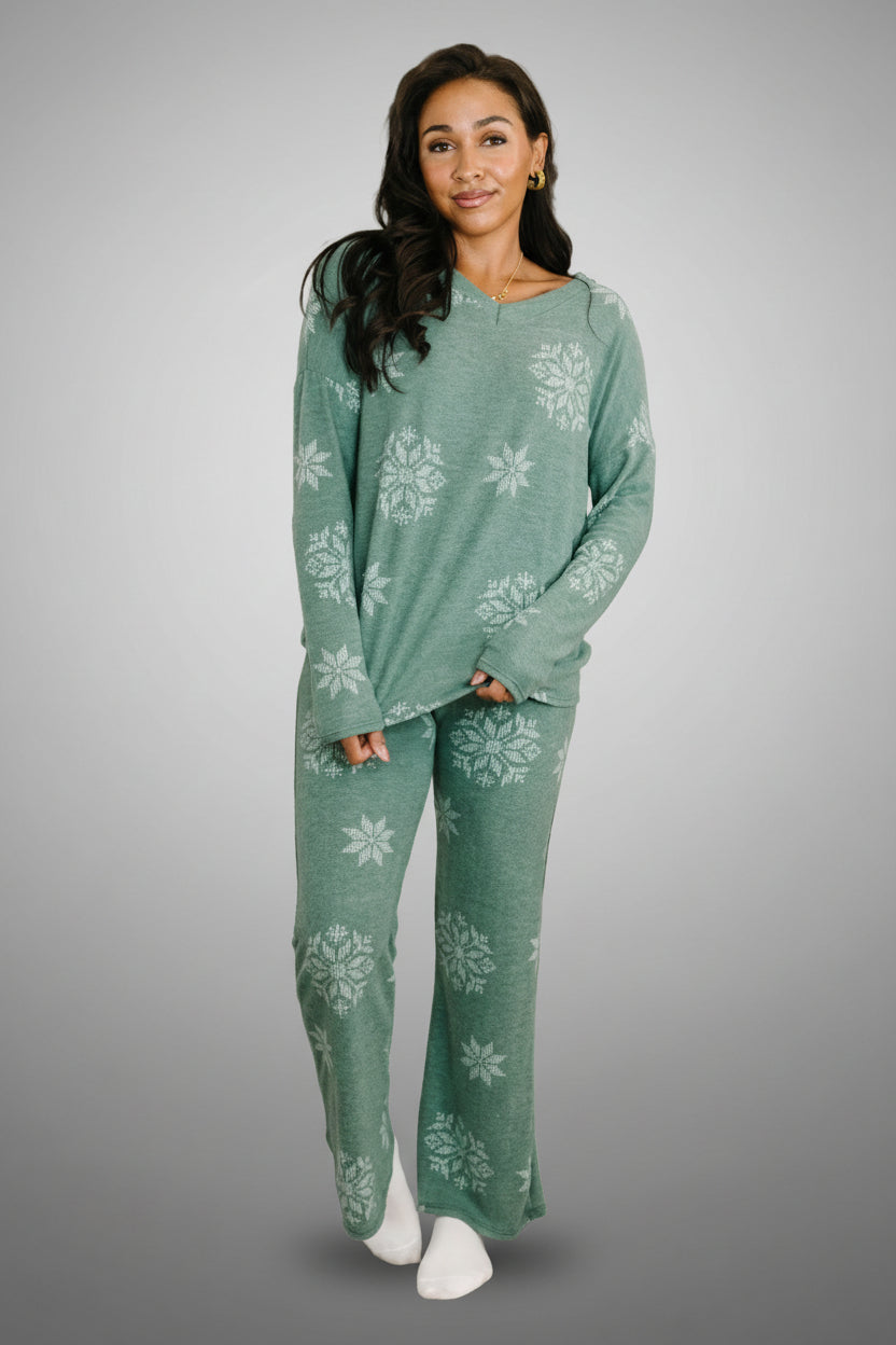 A woman is wearing a matching set that is a faded green and there are multiple-sizes of snowflakes on both.