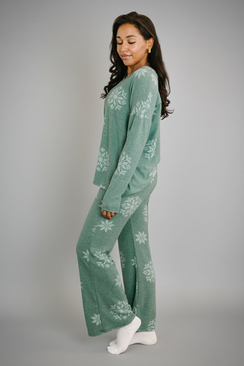 A woman is wearing a matching set that is a faded green and there are multiple-sizes of snowflakes on both.