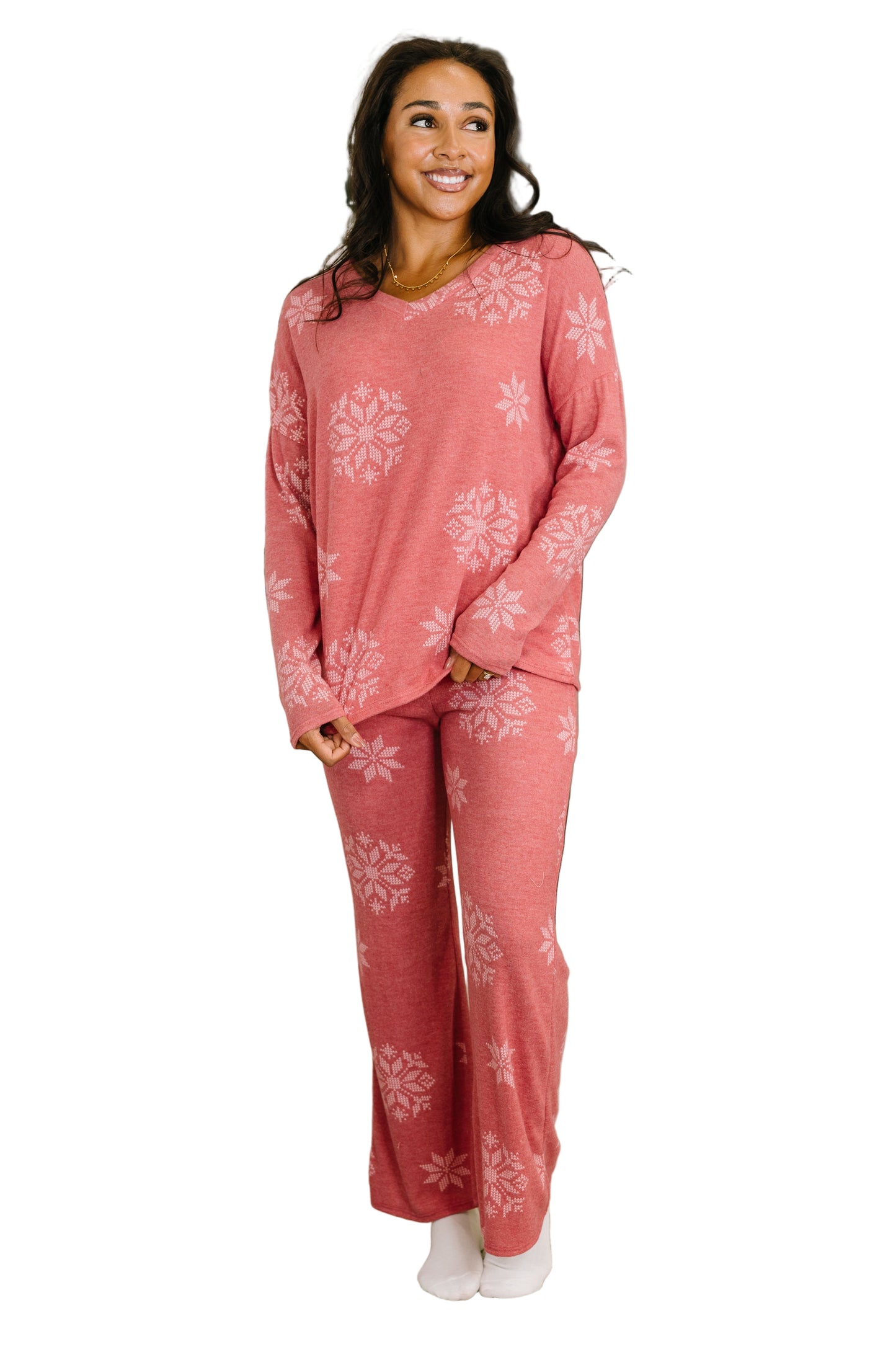 A woman is wearing a matching set that is a faded red and there are multiple-sizes of snowflakes on both.