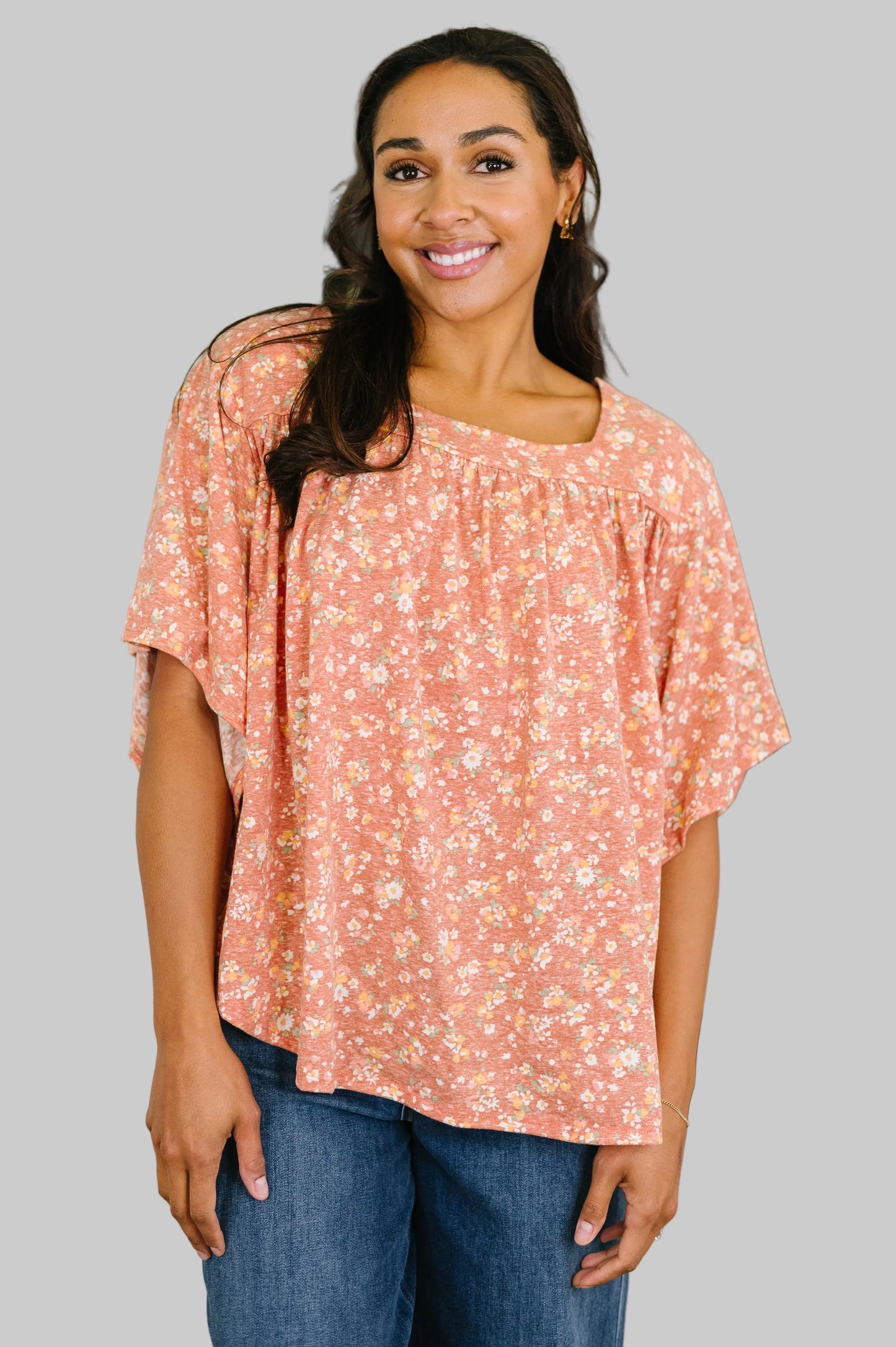 Woman wearing a dusty rose floral square neck top with bell sleeves and boxy relaxed fit, styled with dark wash jeans and gold earrings
