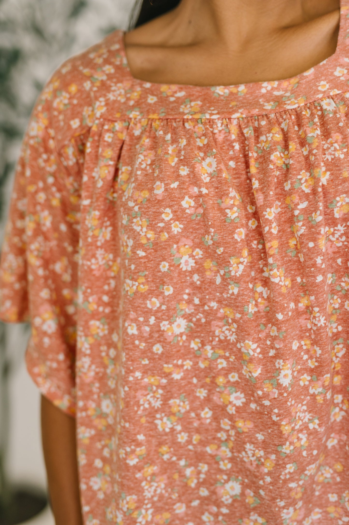 Woman wearing a dusty rose floral square neck top with bell sleeves and boxy relaxed fit, styled with dark wash jeans and gold earrings