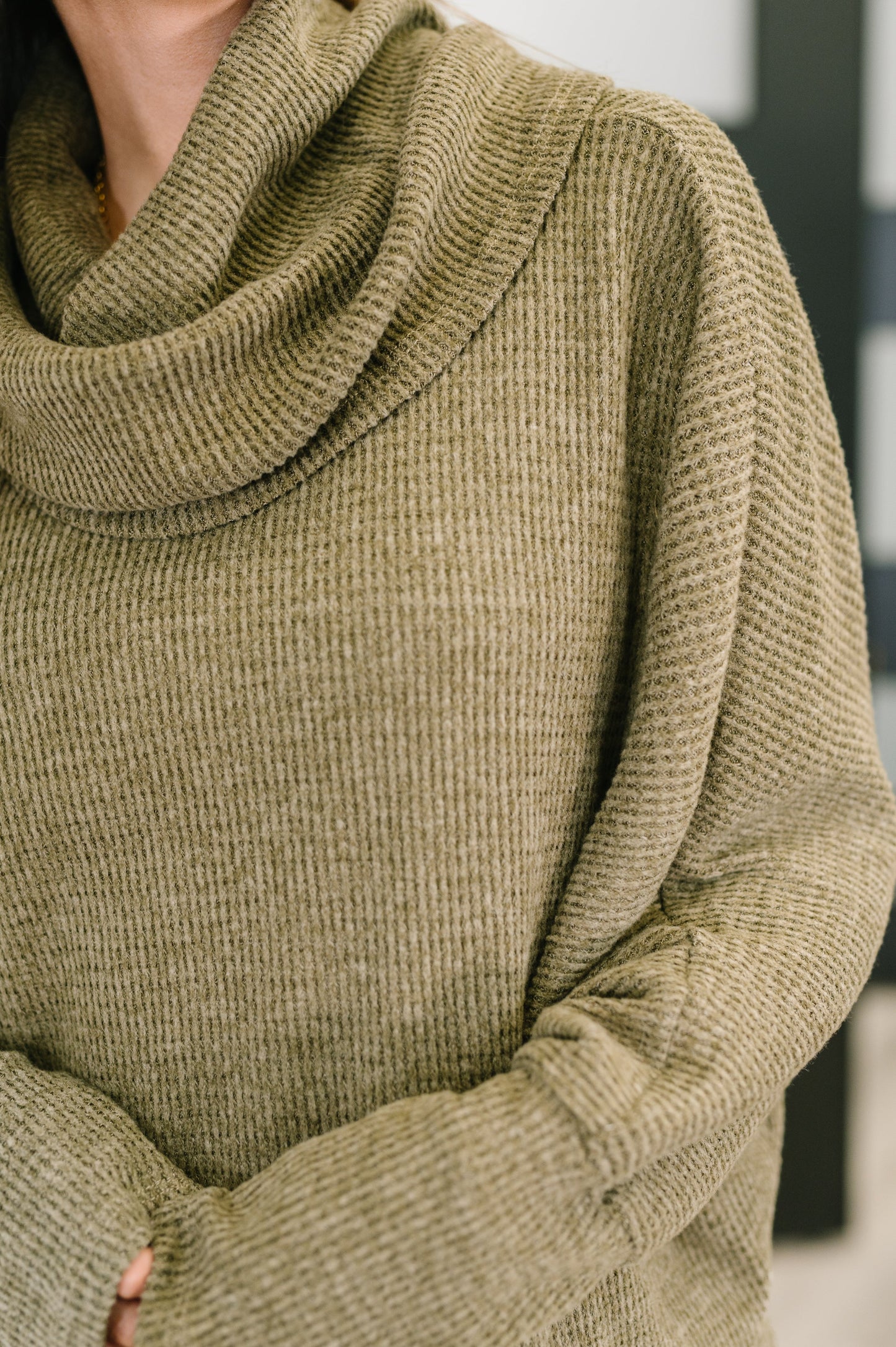Close-up of a person wearing a green knitted sweater with a blurred background