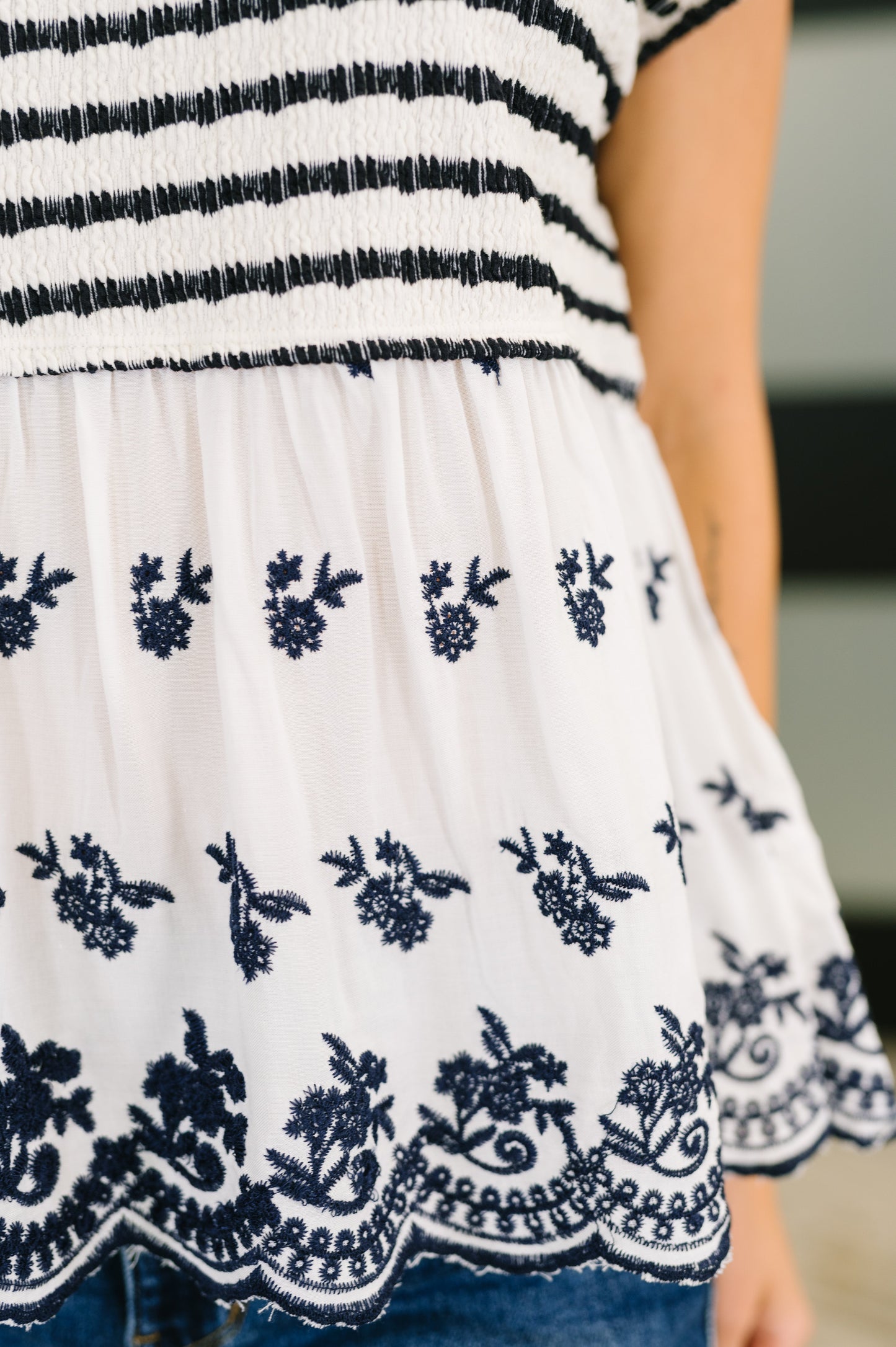 Woman wearing a navy and white striped top with floral lace details, standing indoors.