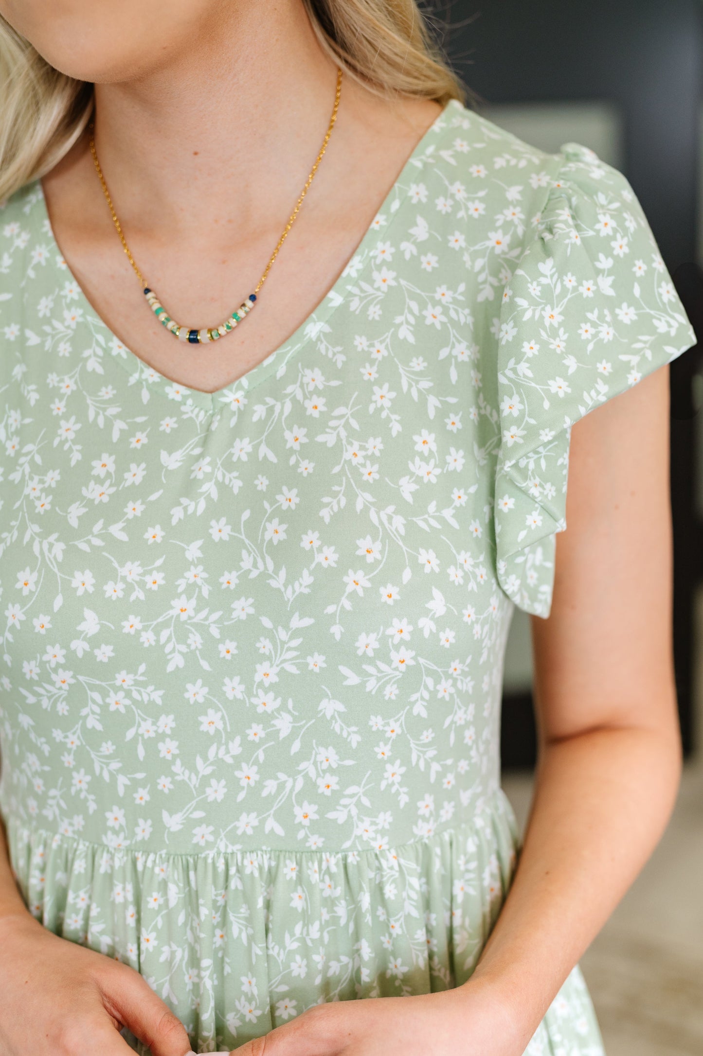 Woman wearing sage green flutter sleeve midi dress with white floral print