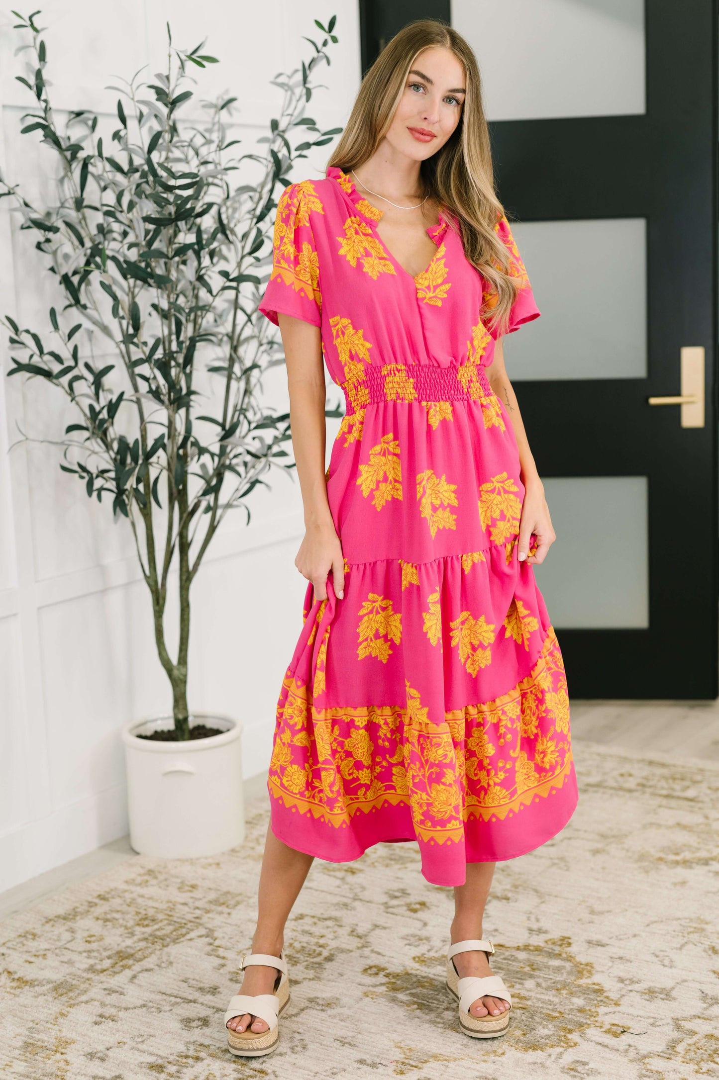 Model wearing fuchsia smocked waist dress with yellow floral print and flutter sleeves