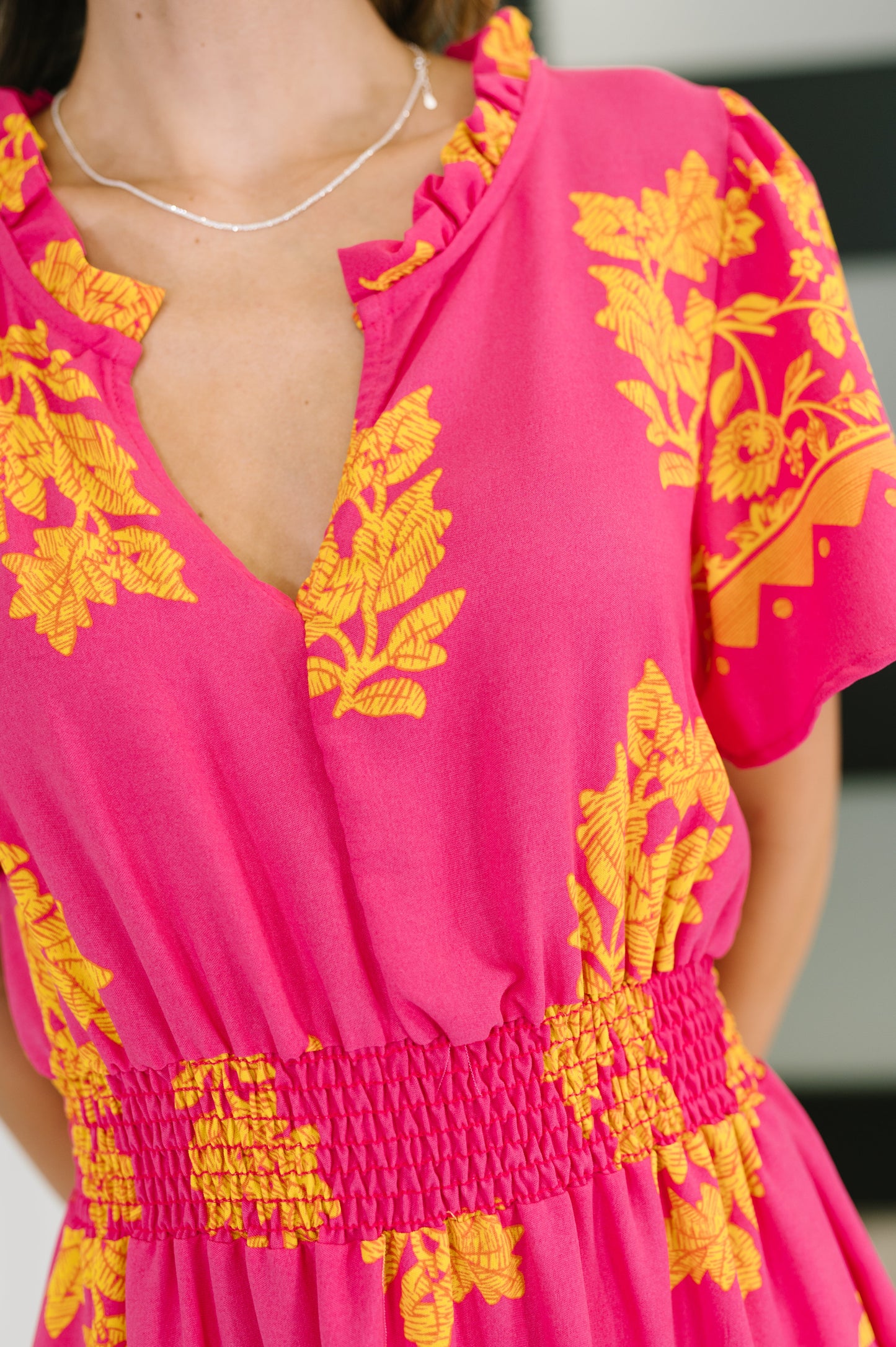 Model wearing fuchsia smocked waist dress with yellow floral print and flutter sleeves