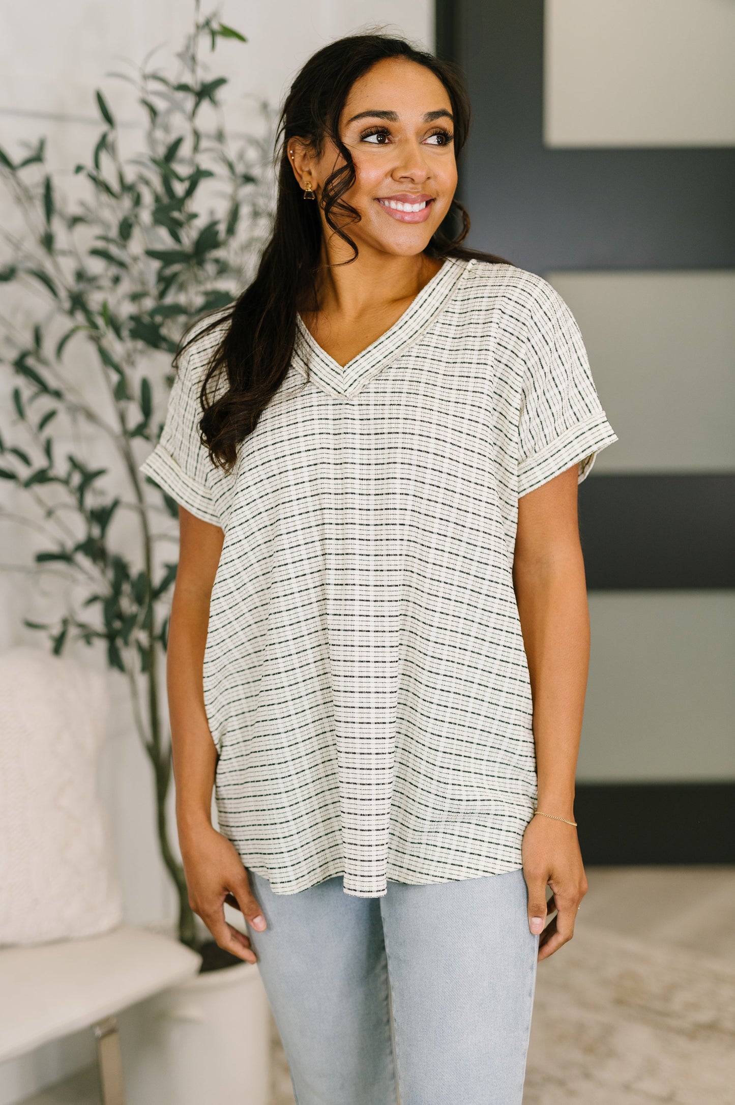 Woman wearing an ivory textured knit v-neck top with subtle dark stripe pattern, banded neckline and cuffed short sleeves, relaxed fit, paired with light wash jeans