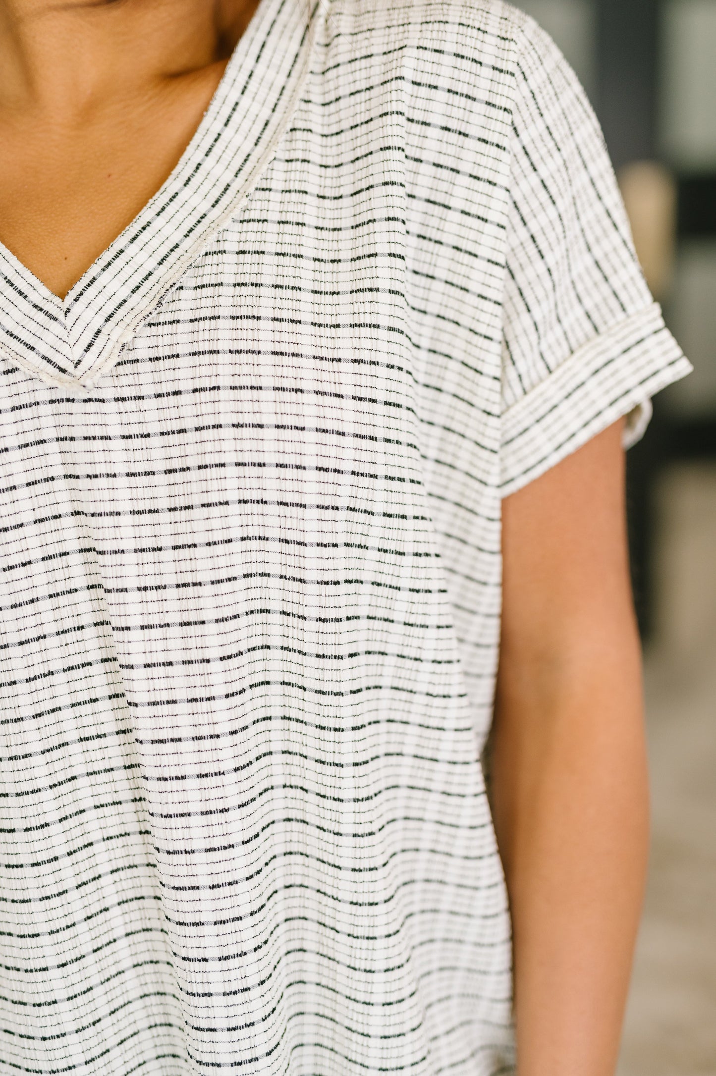 Woman wearing an ivory textured knit v-neck top with subtle dark stripe pattern, banded neckline and cuffed short sleeves, relaxed fit, paired with light wash jeans