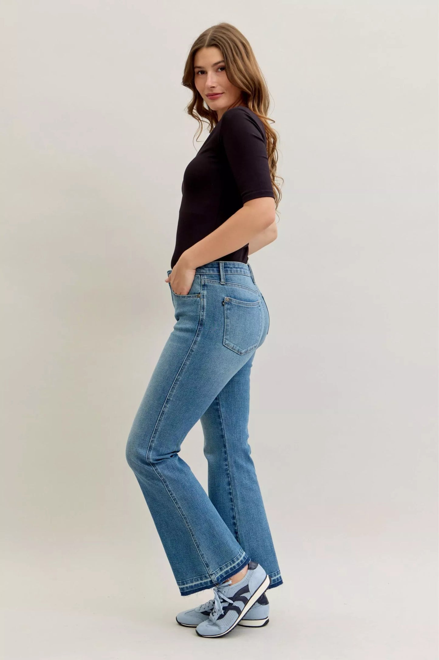 Woman wearing Callie faded medium wash mid rise bootcut jeans with tummy control panel and raw release hem