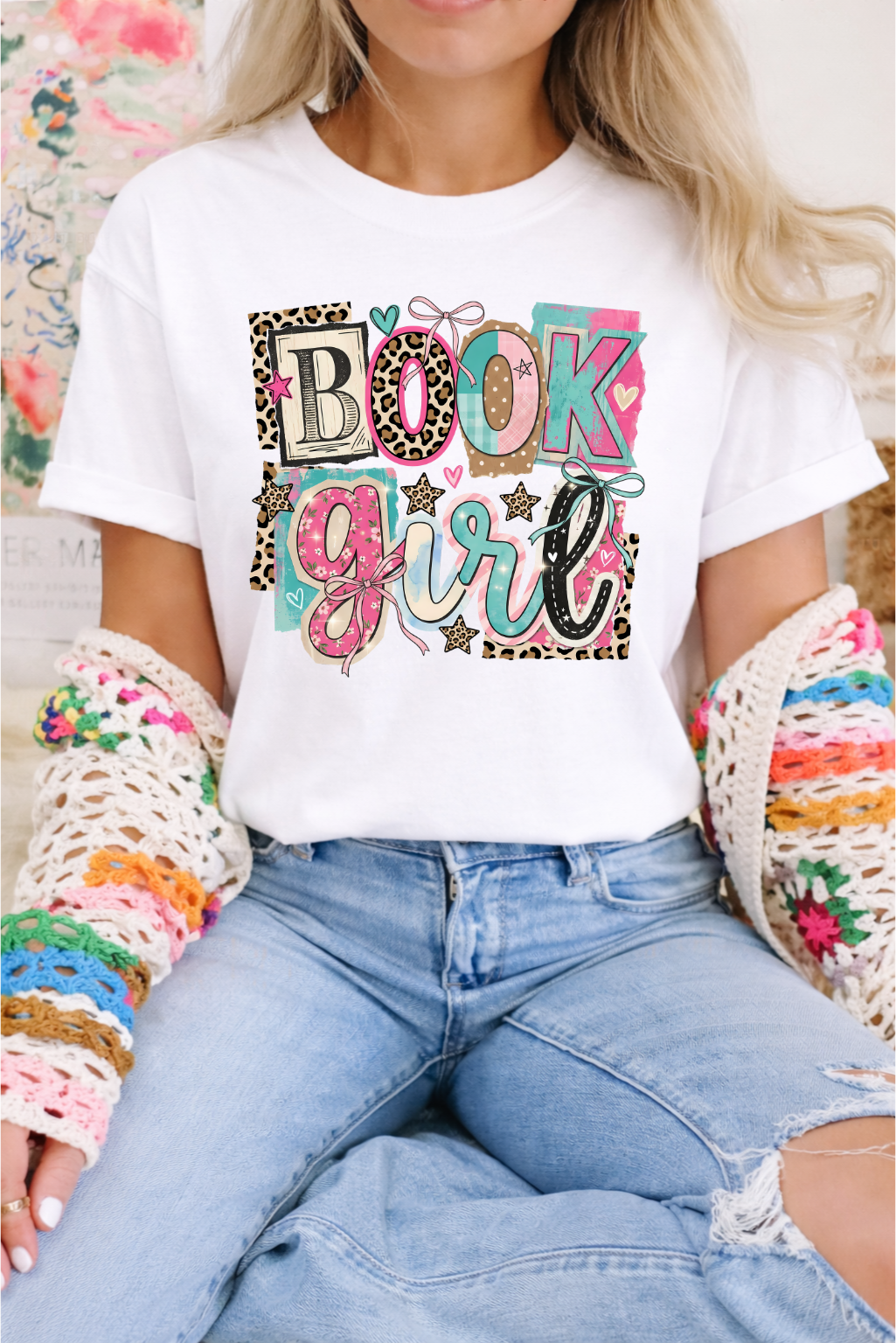 Woman wearing white graphic tee with colorful Book Girl text featuring leopard print, pink bows, stars, and teal accents