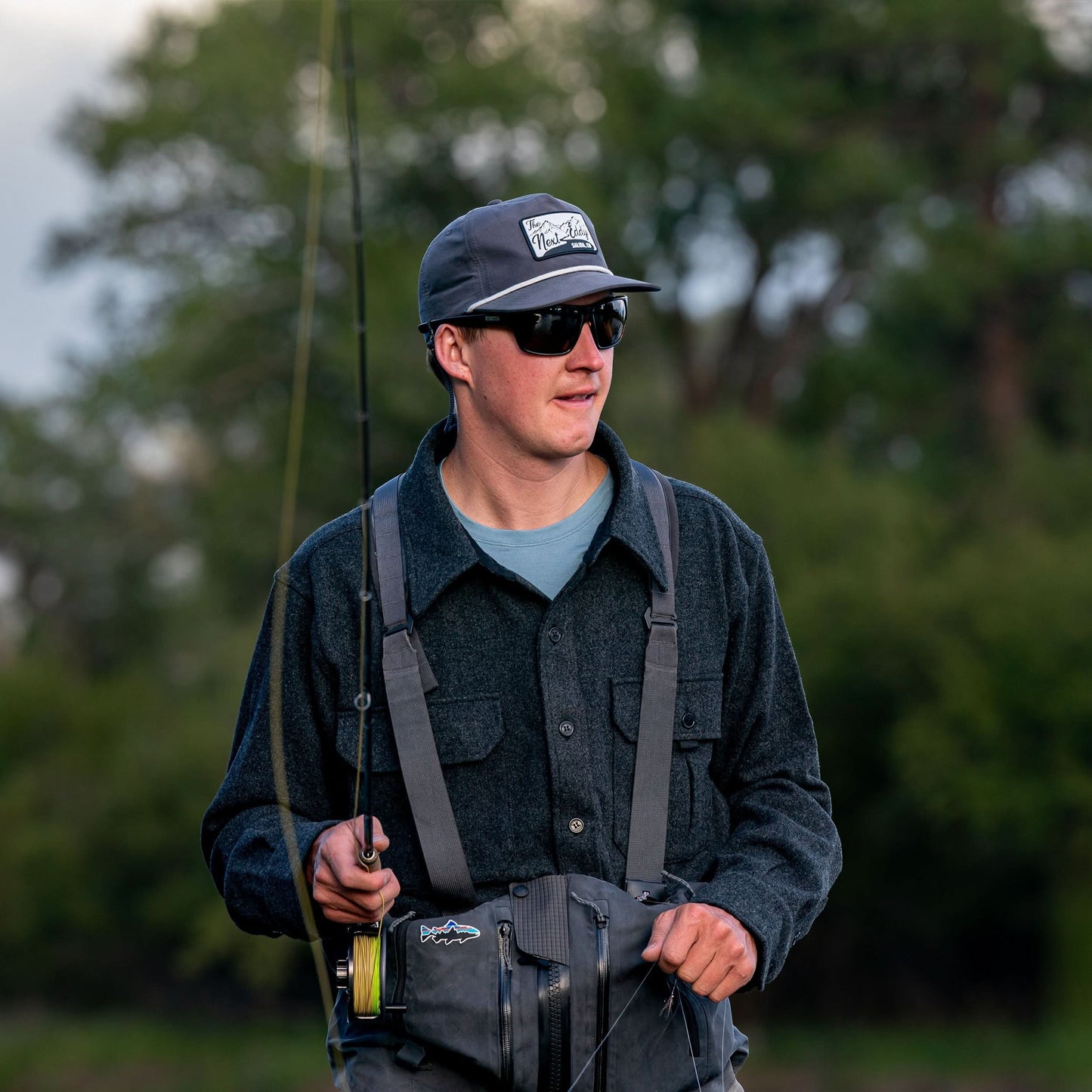 Man in outdoor setting holding a fishing rod and wearing a cap and sunglasses.