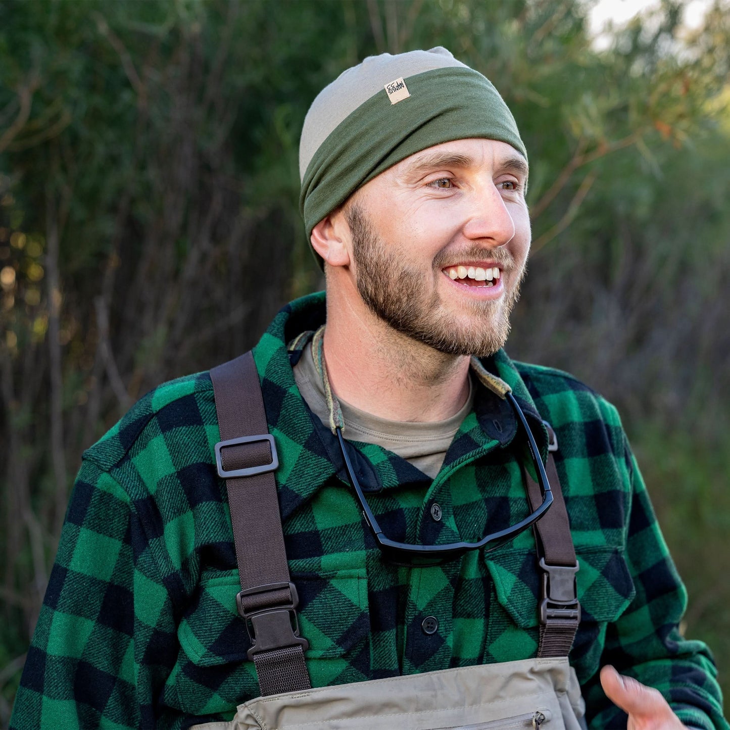 Man wearing a green plaid shirt, suspenders, and a headband outdoors.